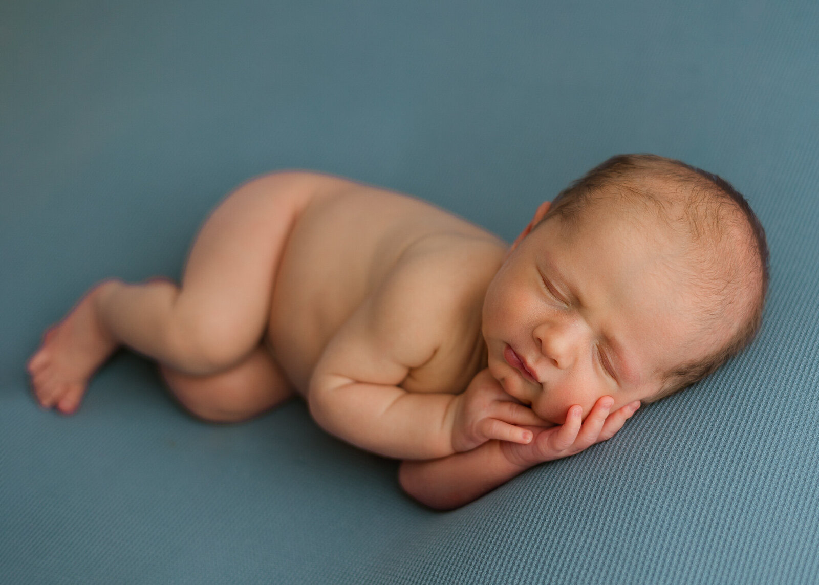 newborn boy in a side laying pose with hands on cheek