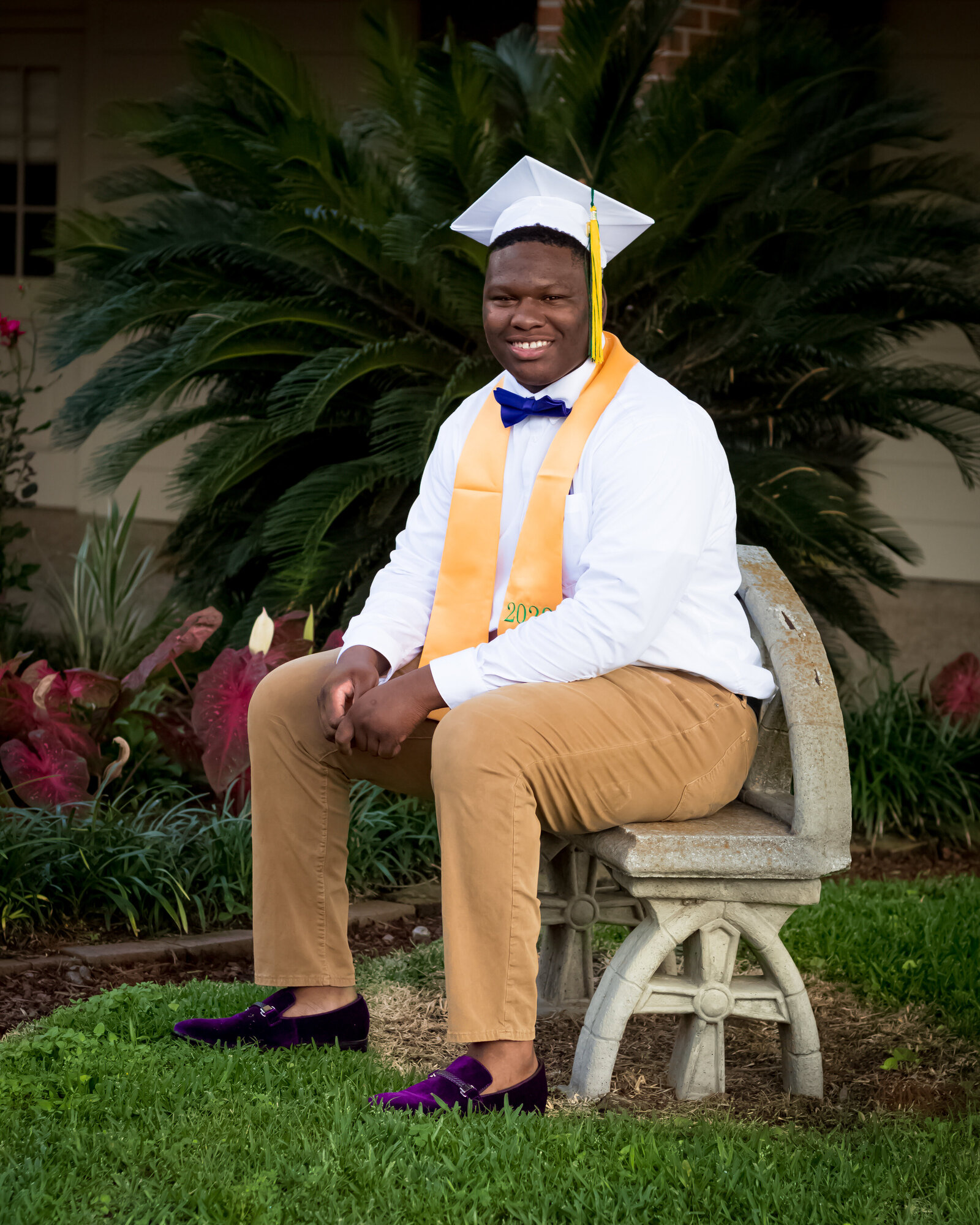 boy sitting on bench wearing graduation cap and stole