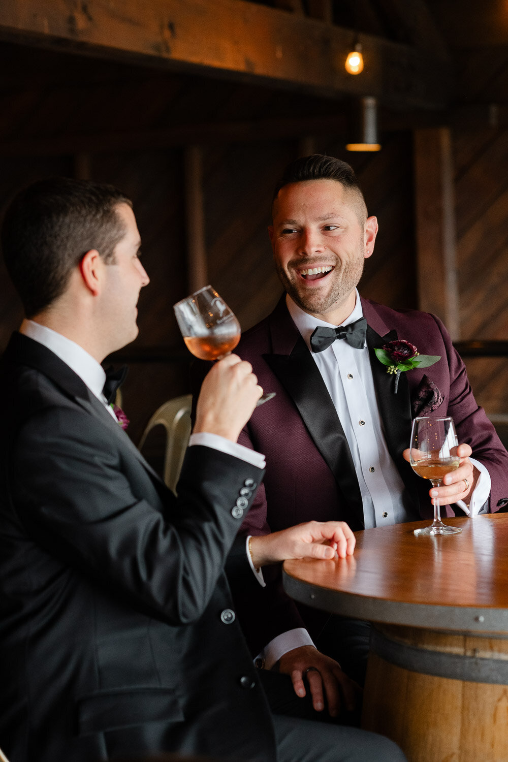 grooms sitting at table drinking wine at vineyard