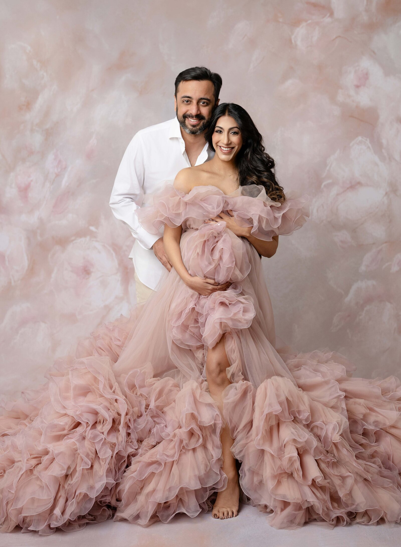 Mom dressed in pink maternity gown and Dad holding her belly. Photo was taken at Luxury Maternity photo studio in Atlanta, GA.