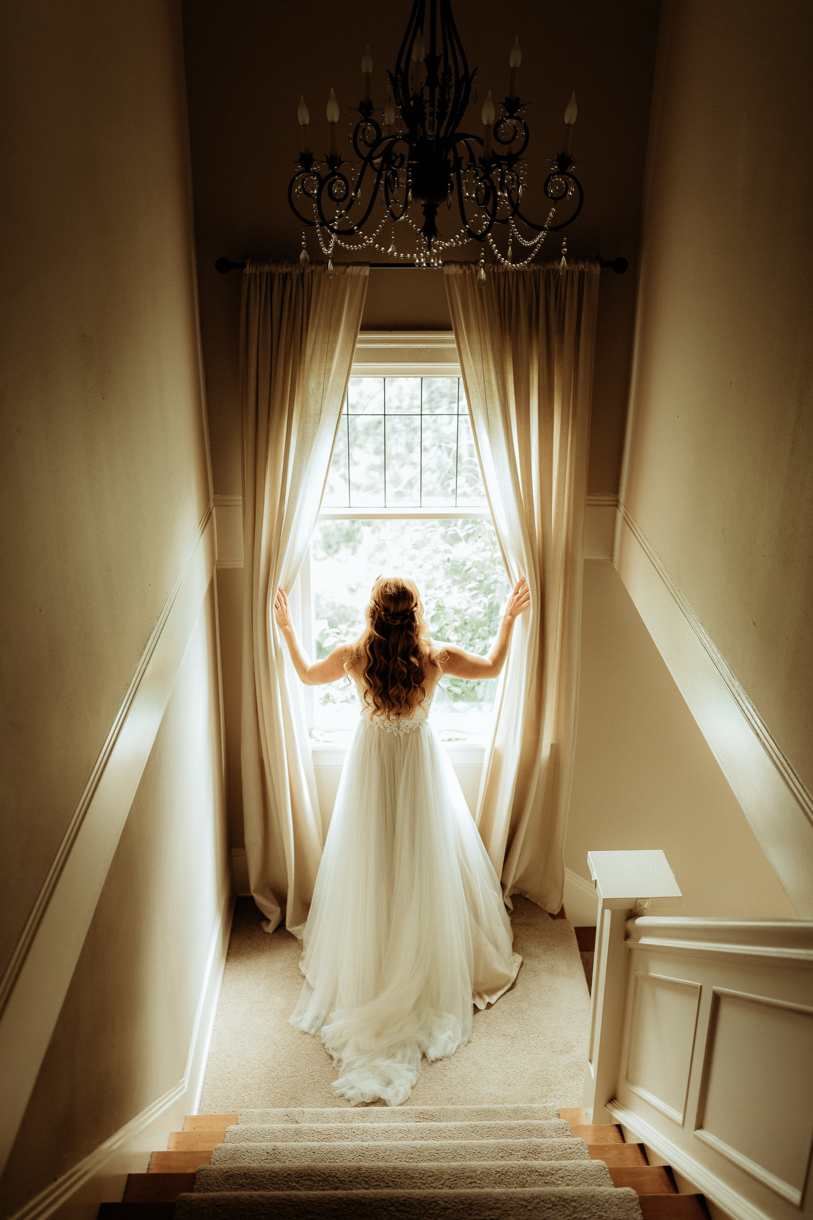 Bride standing in front of a window at the middle landing of a stairway