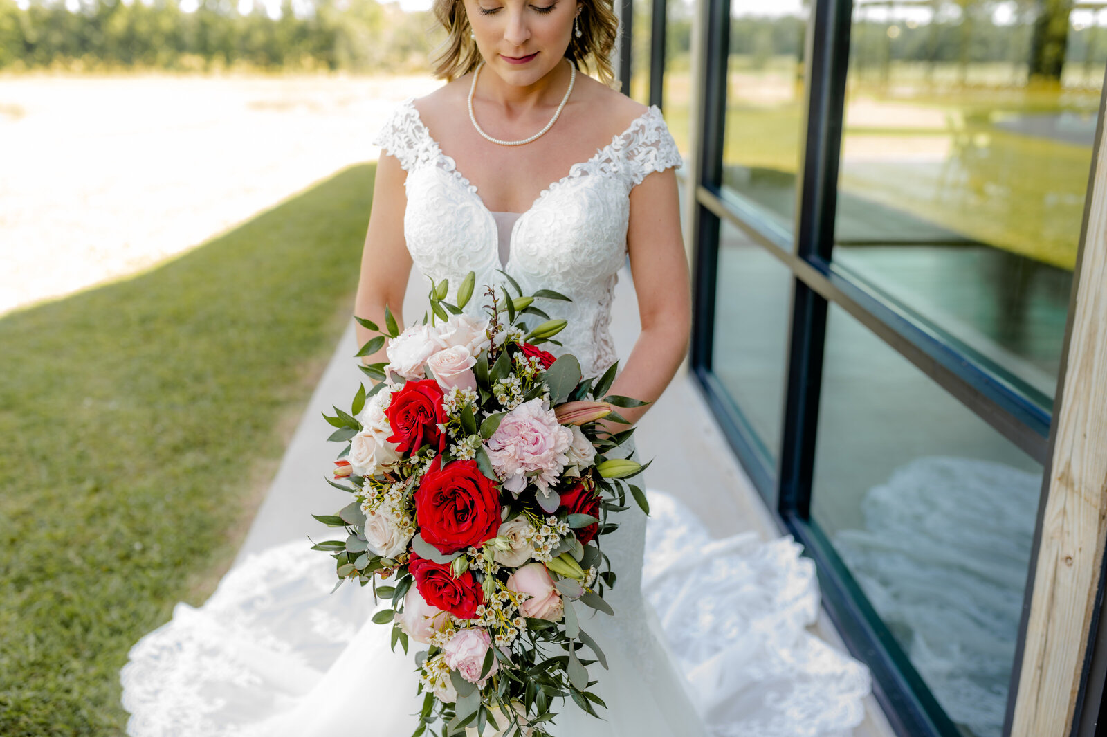 little rock ar wedding photographers capture bride holding her red, pink and white wedding bouquet outside of her wedding venue for her summer wedding