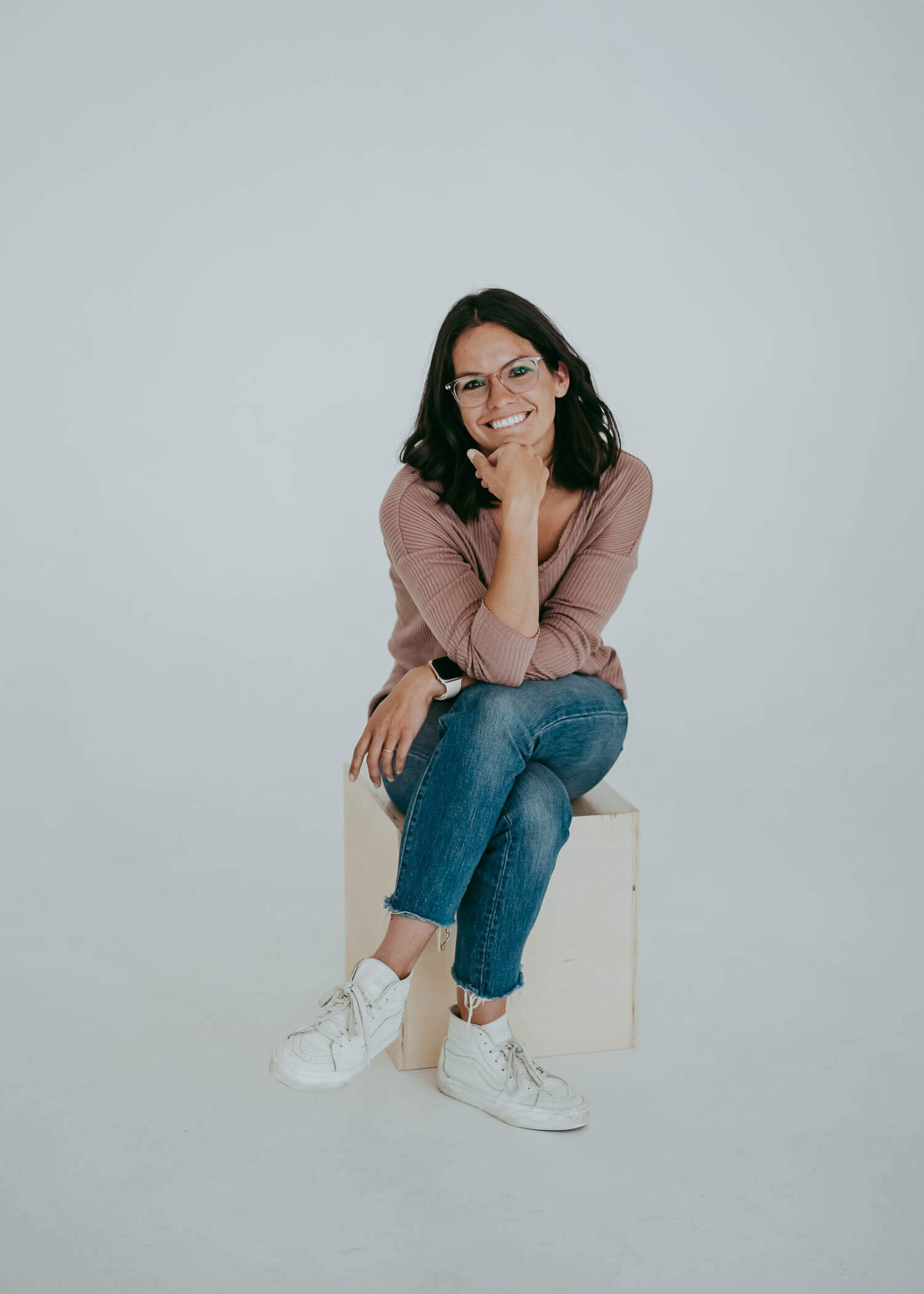 A graphic designer comfortably sits on a store with her legs crossed wearing denim and a mauve colored shirt, while looking directly at the camera during her Denver branding session.
