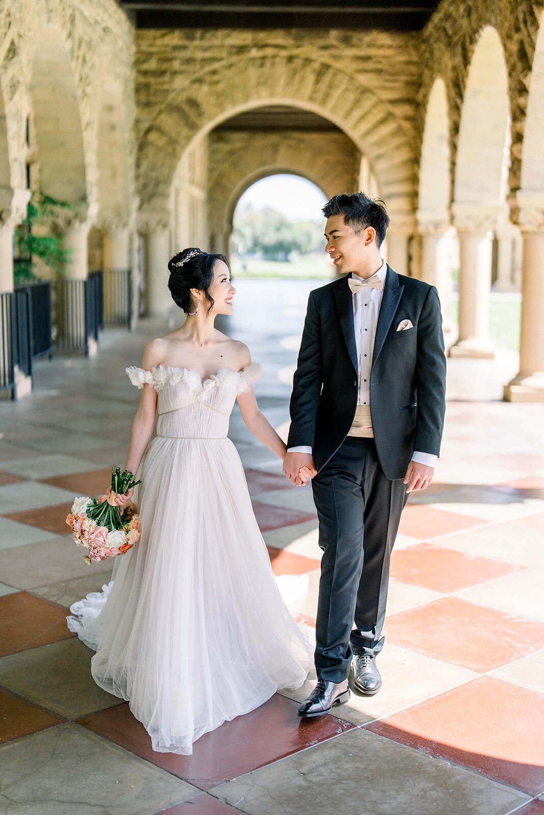 The bride and groom enjoy a romantic stroll through the beautiful archways of Stanford University, capturing the elegance and charm of their special day.