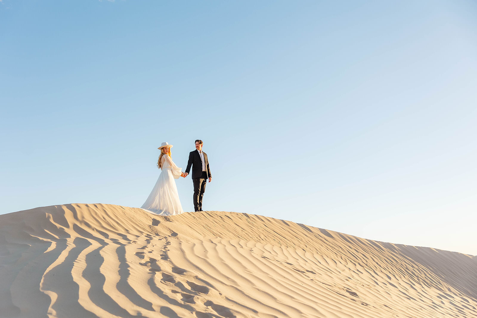 Couple eloping hand in hand atop the stunning sand dunes in Utah, capturing their love in a breathtaking desert landscape.