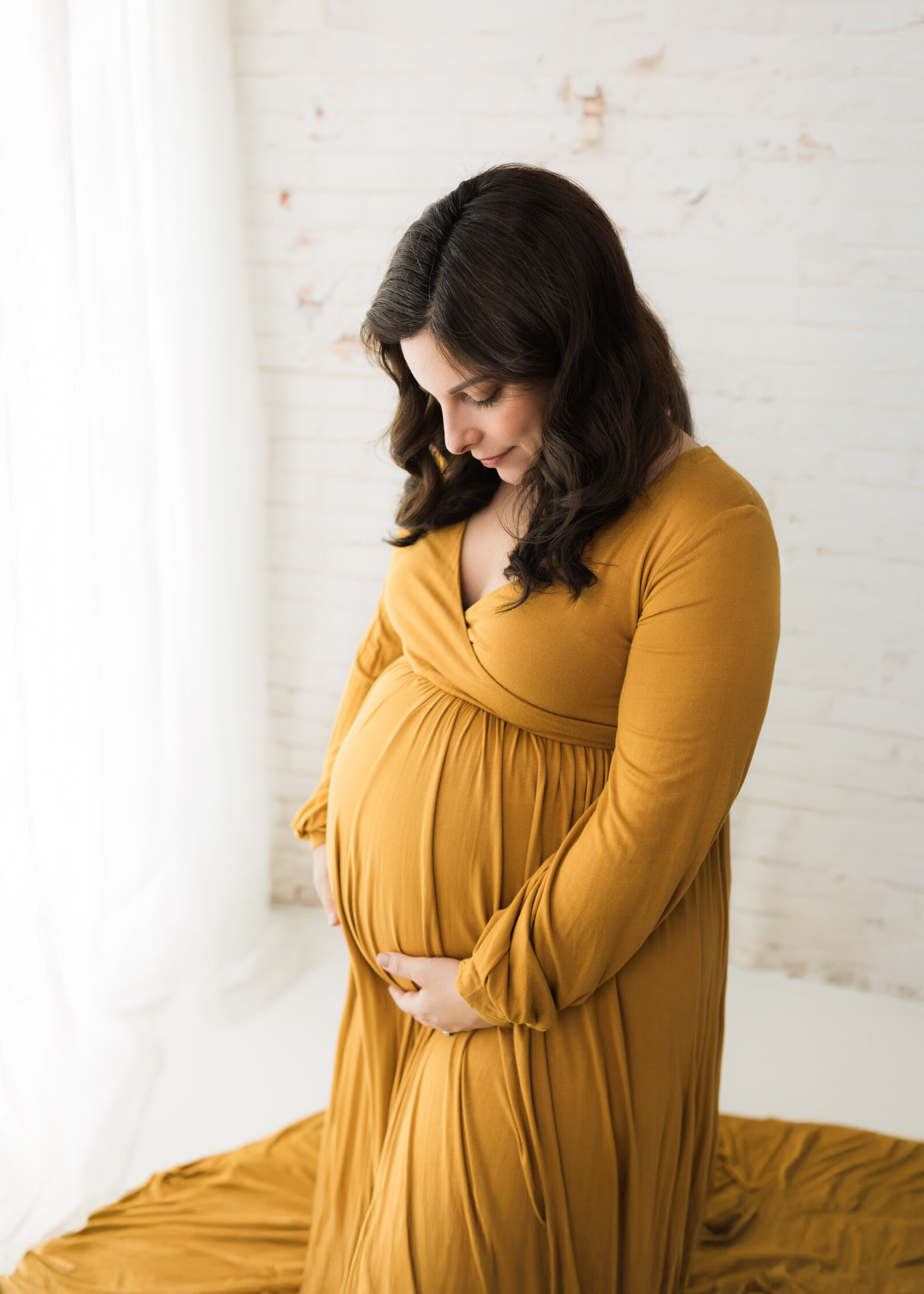 pregnant mother in mustard colored dress holding belly for maternity photoshoot Cleveland maternity photographer