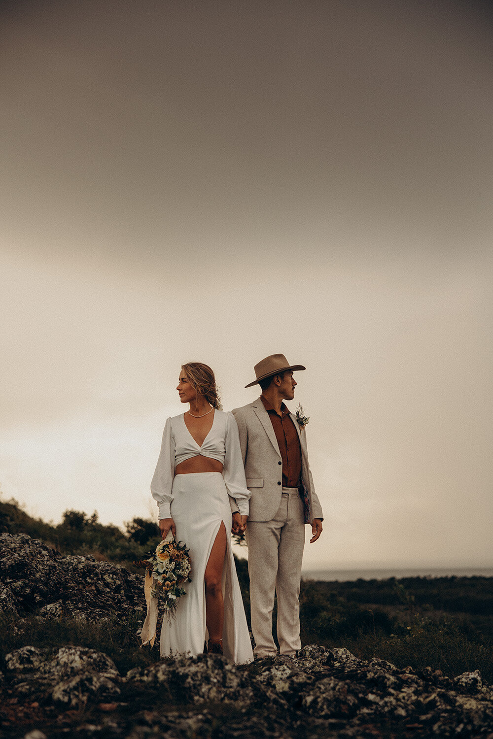 Bride and groom standing on a rocky clifftop with dramatic skies behind them, captured by Sunshine Coast elopement photographer.