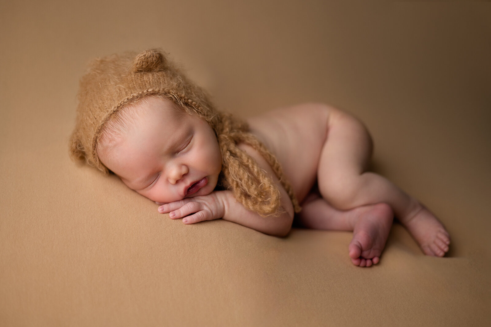 Newborn baby boy  in bear bonnet posed on his side on  a tan backdrop