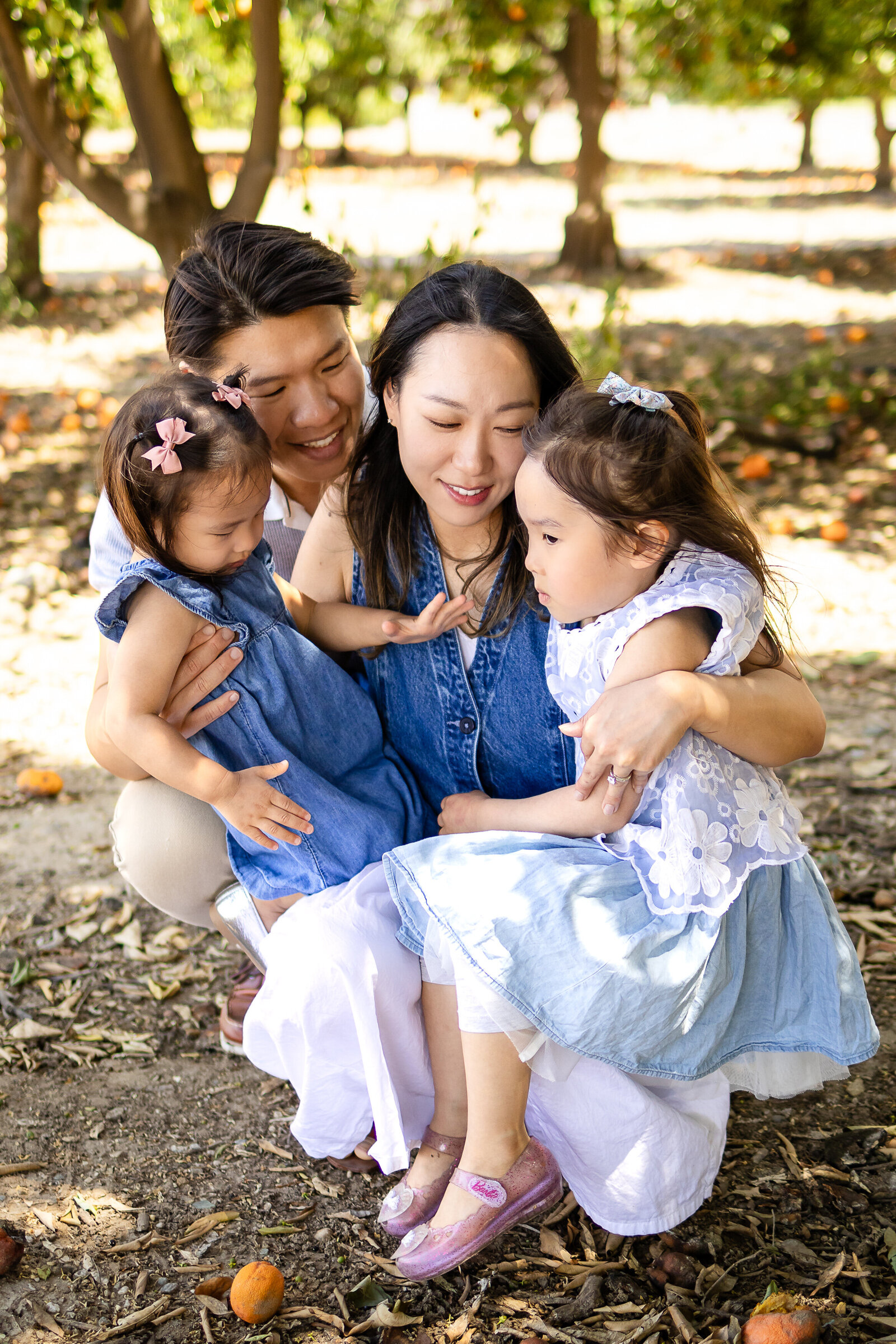 Parents lovingly embracing their two young daughters during a relaxed outdoor session with Ellobelle Photography.