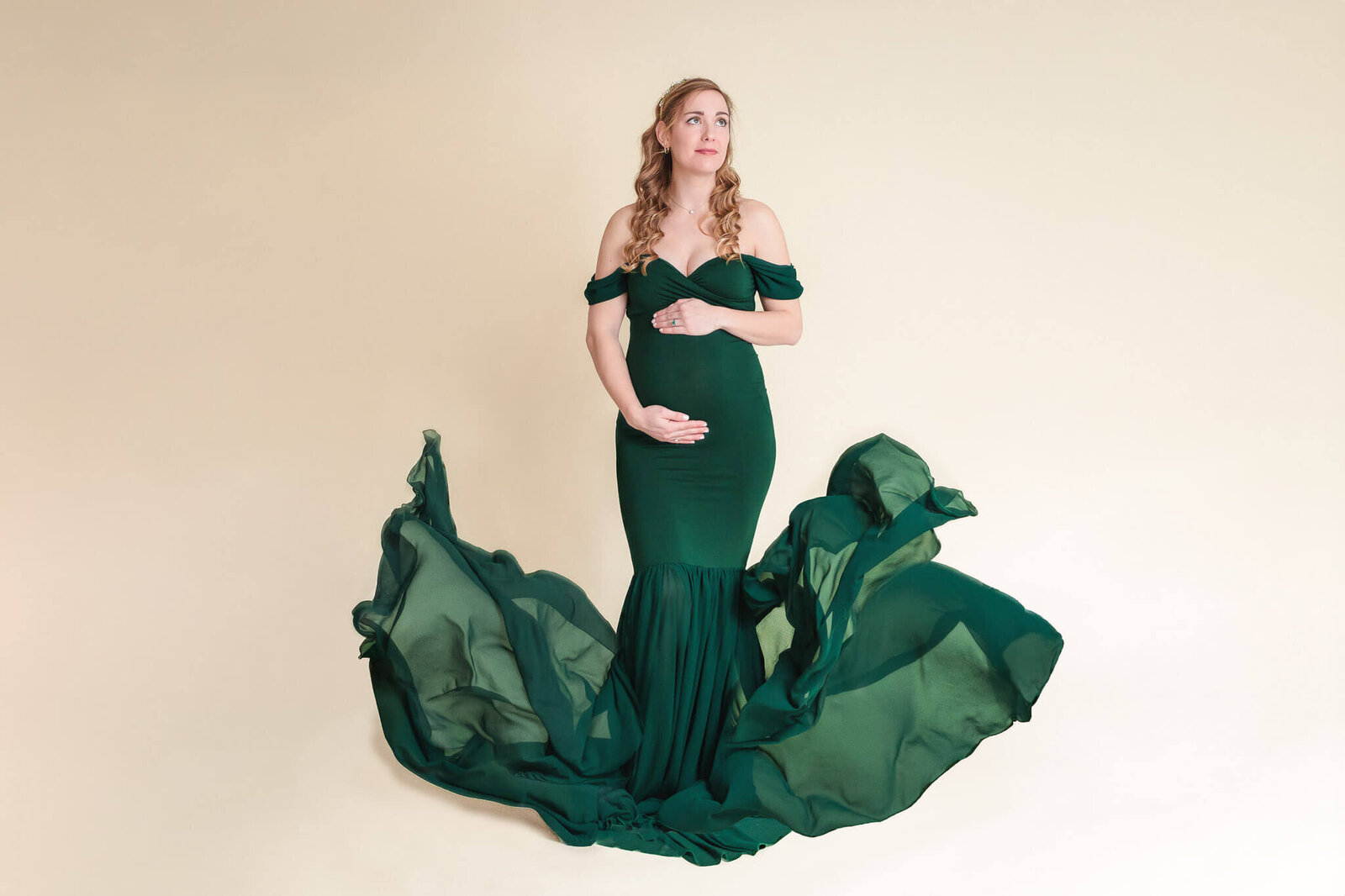 A pregnant woman hugging her belly while her dress train flies on both sides of her.