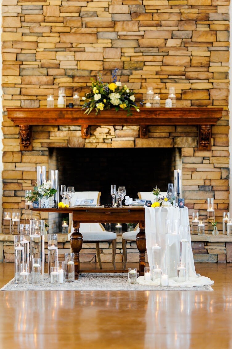 The sweetheart table decorated with white linen draping, floating candles, and floral arrangements in front of the great fireplace at The Summit at Willow and Stone Events, NC