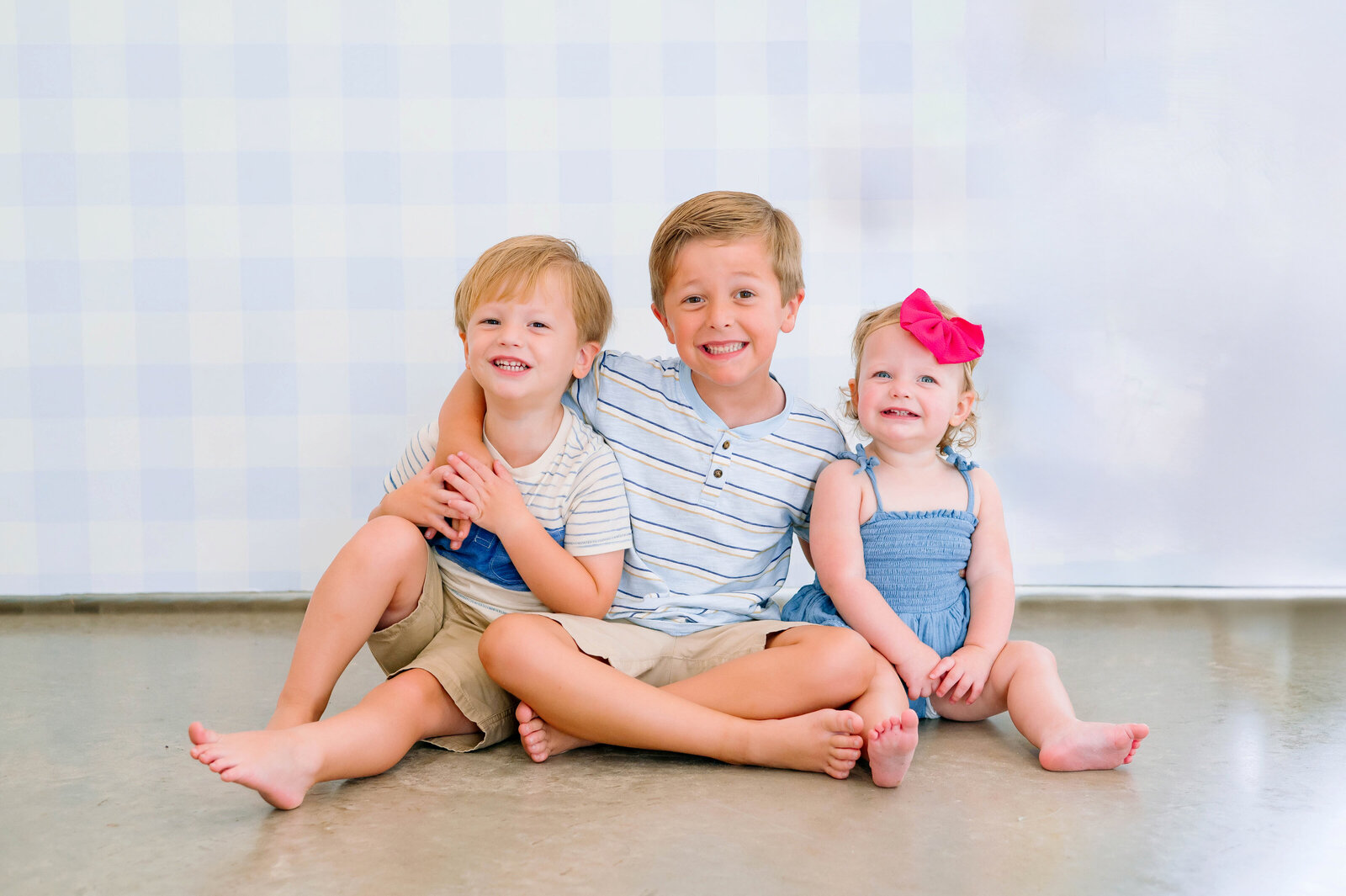 Two young siblings smiling during a light and airy studio portrait session in Plano, Texas, photographed by Jennifer L. Kirk Photography.
