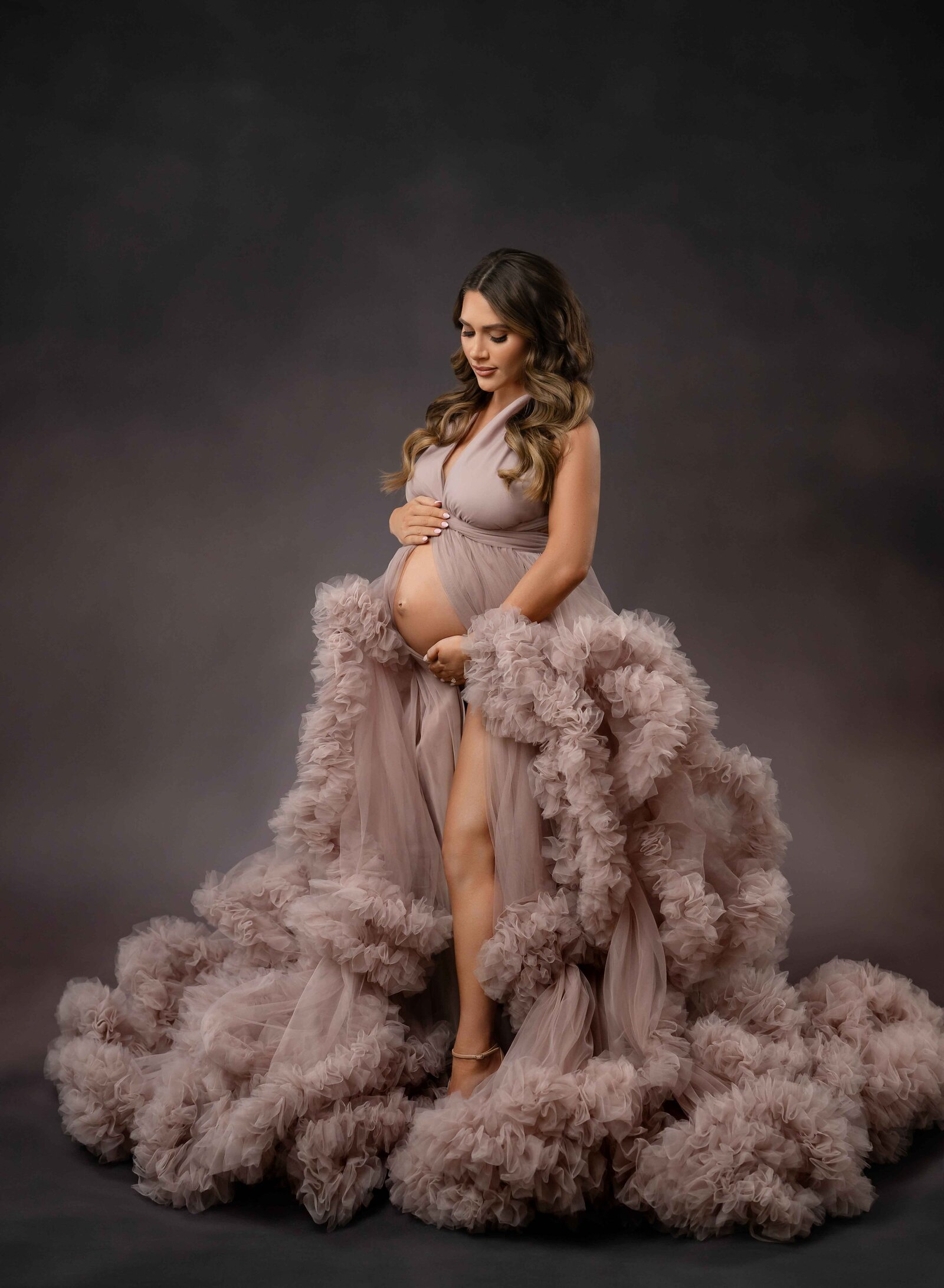 pregnant women in mauve maternity gown, standing up and looking down at her belly bump. Photographed by Atlanta photographer.