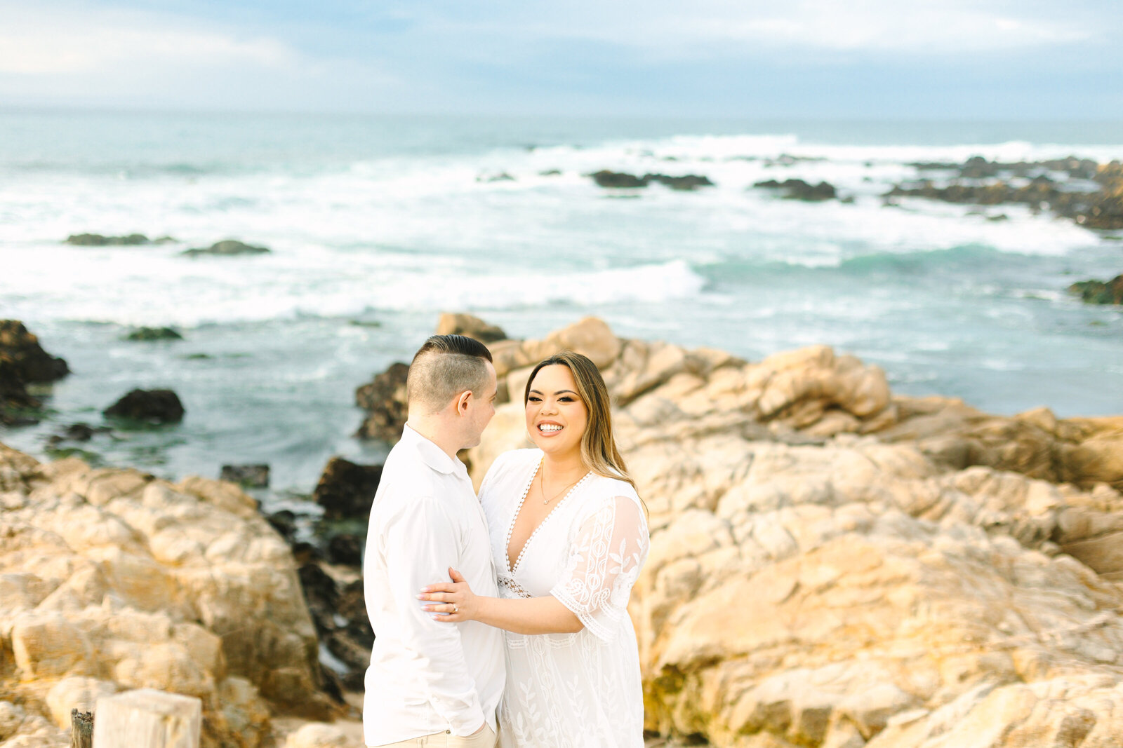 An engaged man and woman take photos on the beach in Pacific Grove, Monterey, California near Big Sur.
