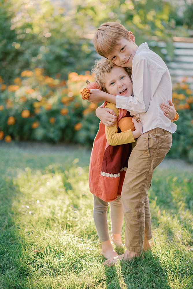 Brother and sister hugging each other in the garden while holding tiny pumpkins