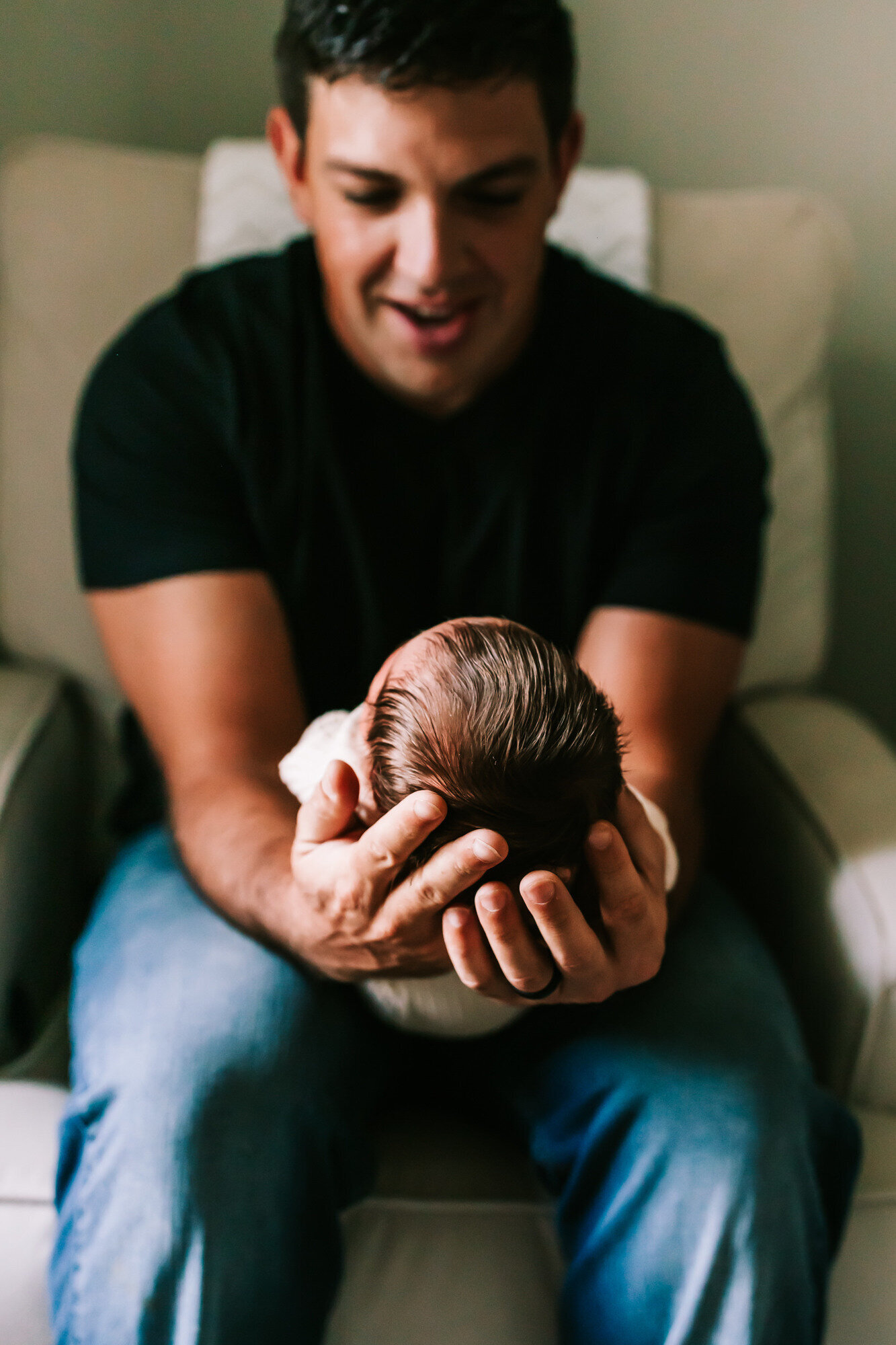 father holding newborn child looking down on child and smiling
