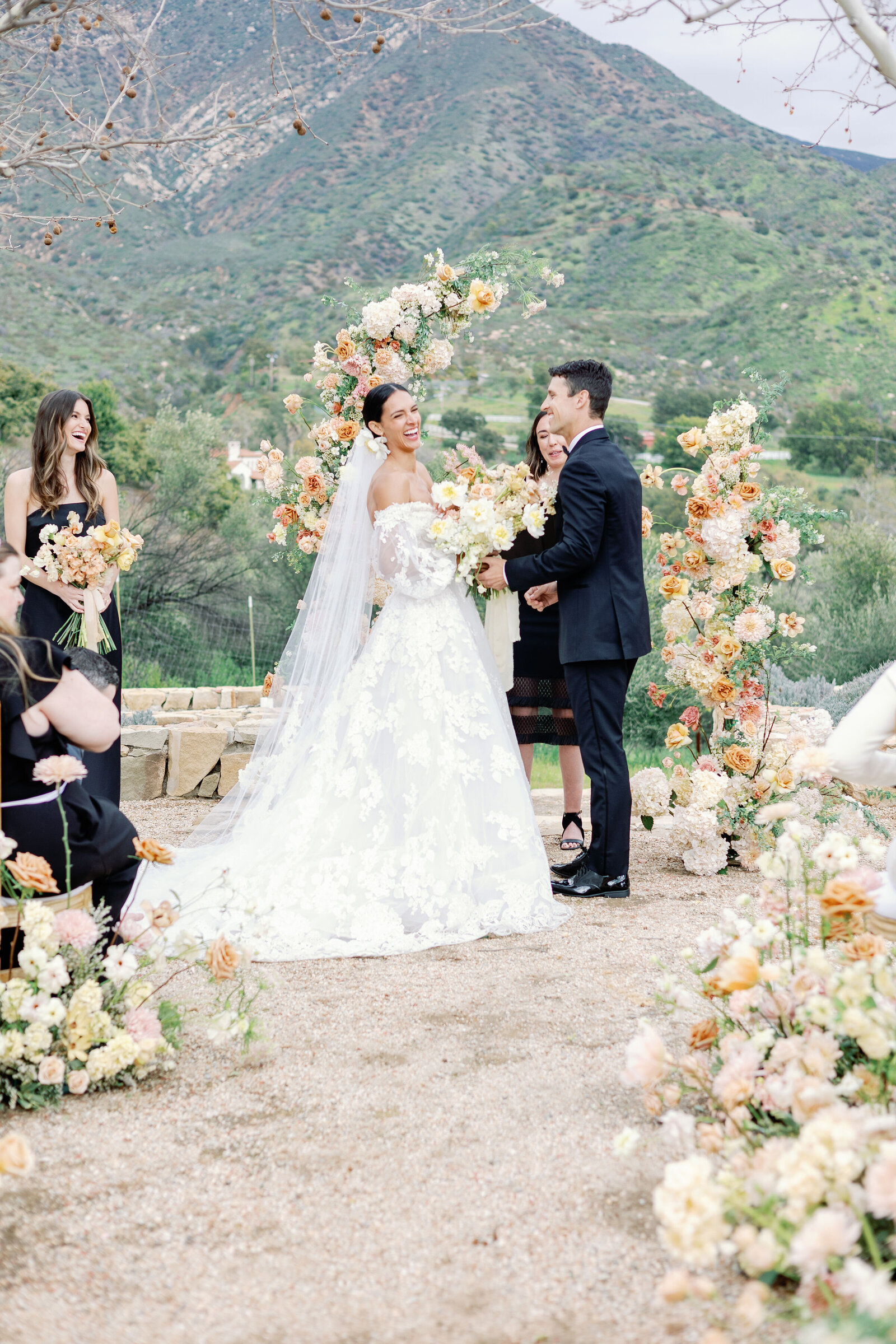 wedding photographer bay area photographs bride and groom standing together sharing their vows together while the bride laughs with a view of the valley behind them for their Ojai wedding