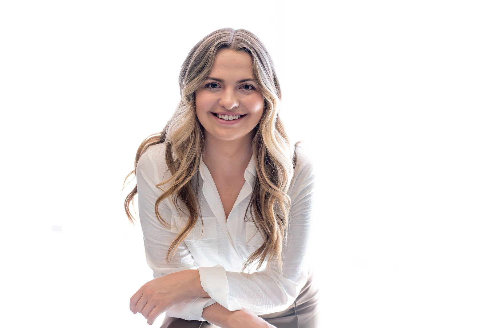 Smiling woman with long wavy hair wearing a white blouse in a bright studio setting, photographed by Vyrl Photo for Tucson headshots.