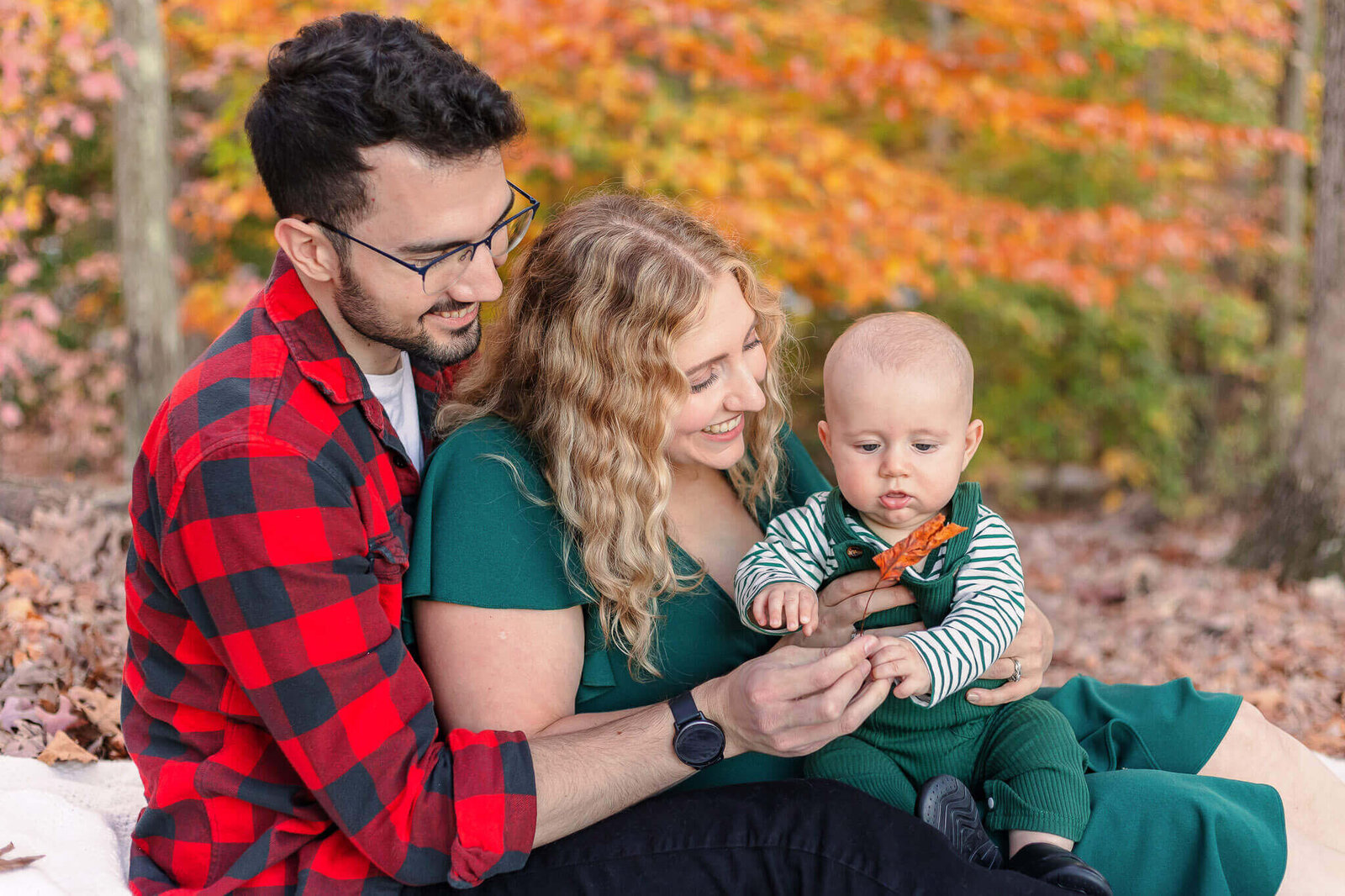 A Northern Virginia family sitting on the floor and playing with a leave among the fall foliage.