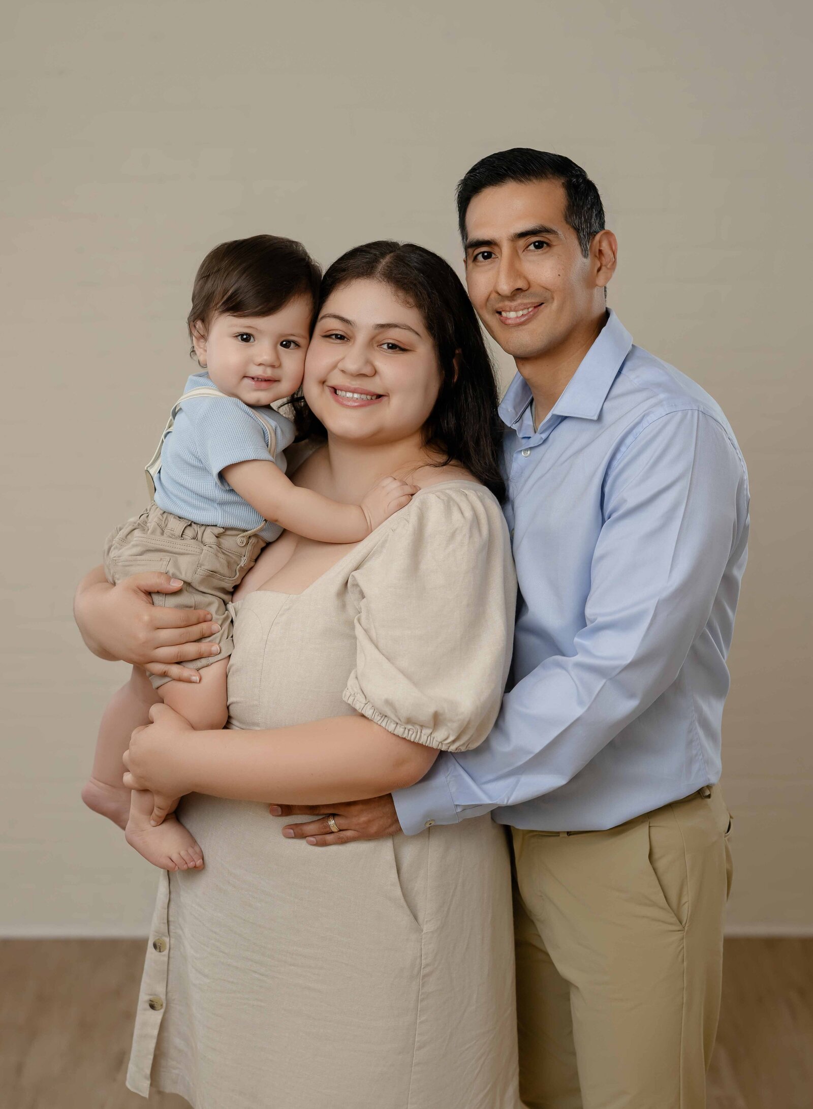 Family portrait in photo studio with Mom holding baby and Dad hugging in behind Mom. 