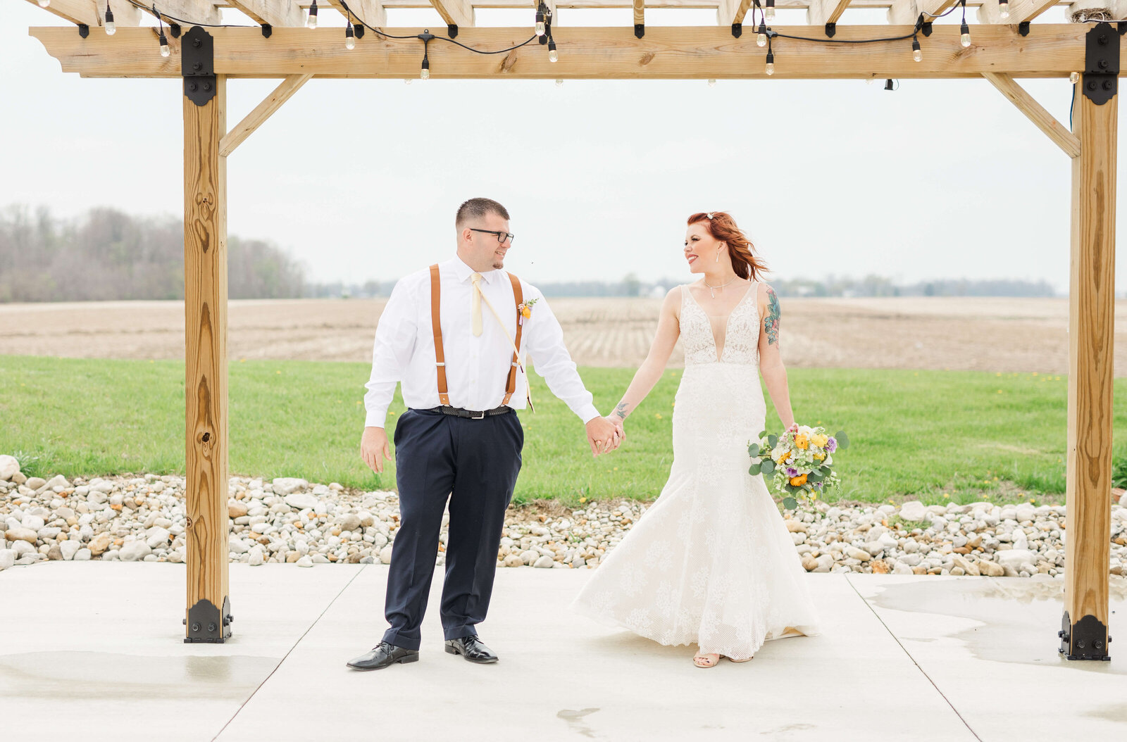 A groom holds hands with his bride as they stand under a gazebo at Blessing Barn. capture by ohio wedding photographer.