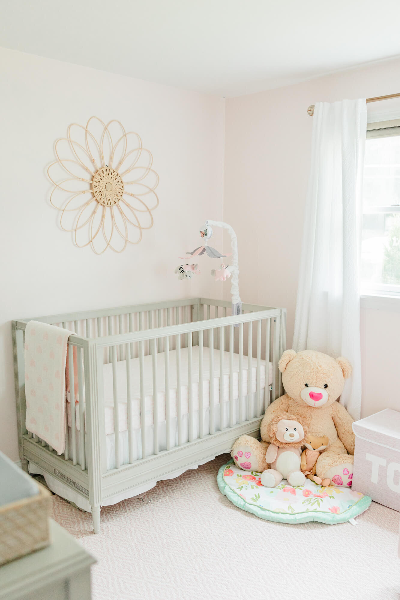 Pink nursery with crib, flower on the wall, and stuffed animals