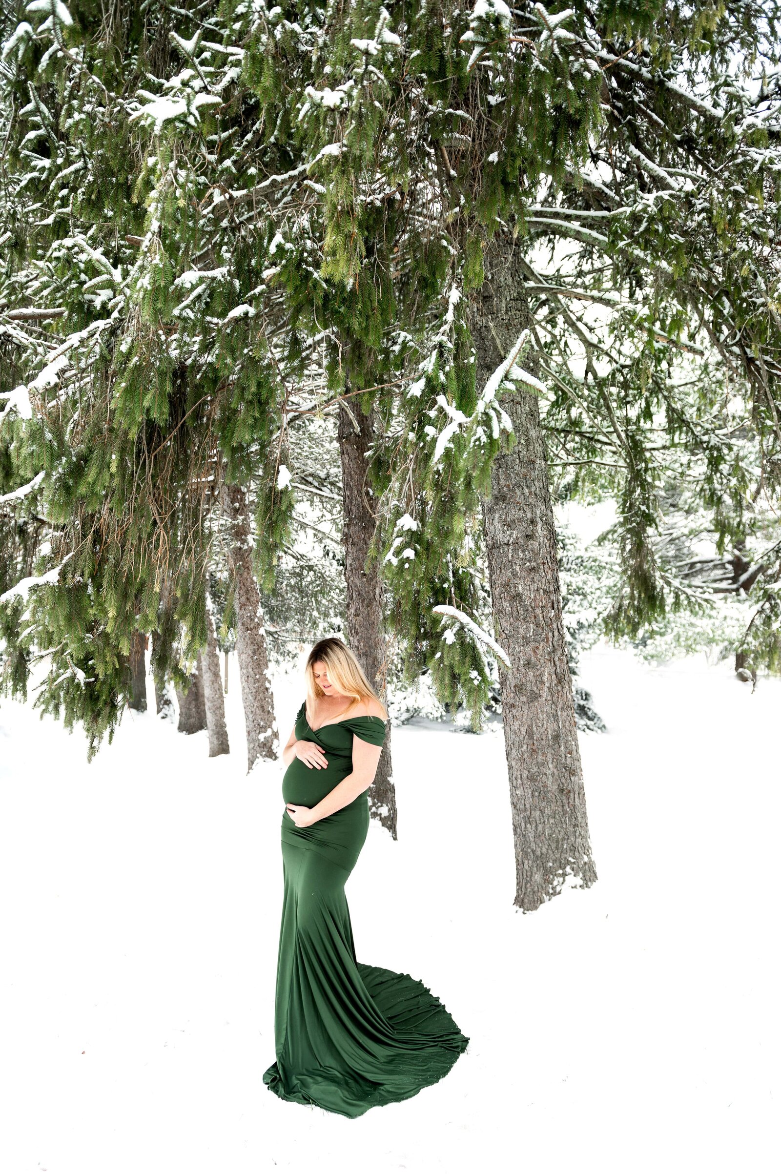 woman in the snow for a maternity session in a green dress