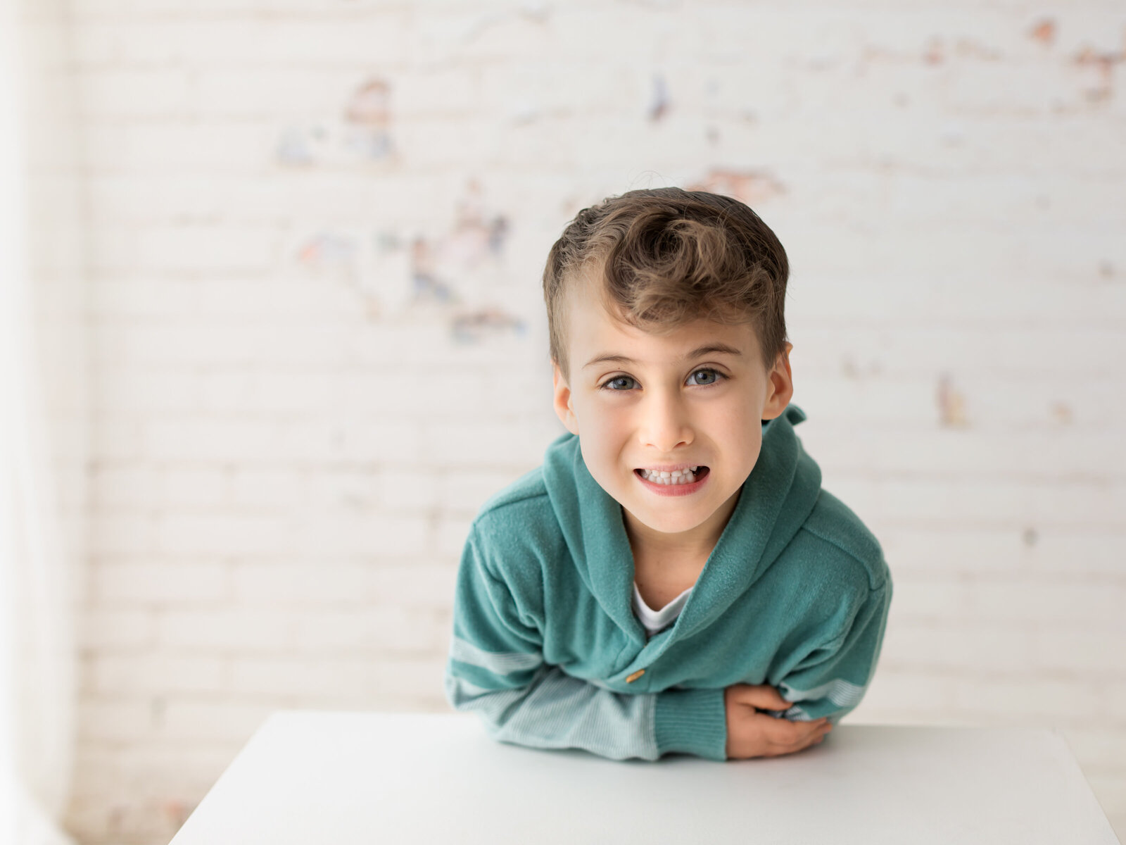 Little boy in green sweater posing on white block for birthday photoshoot