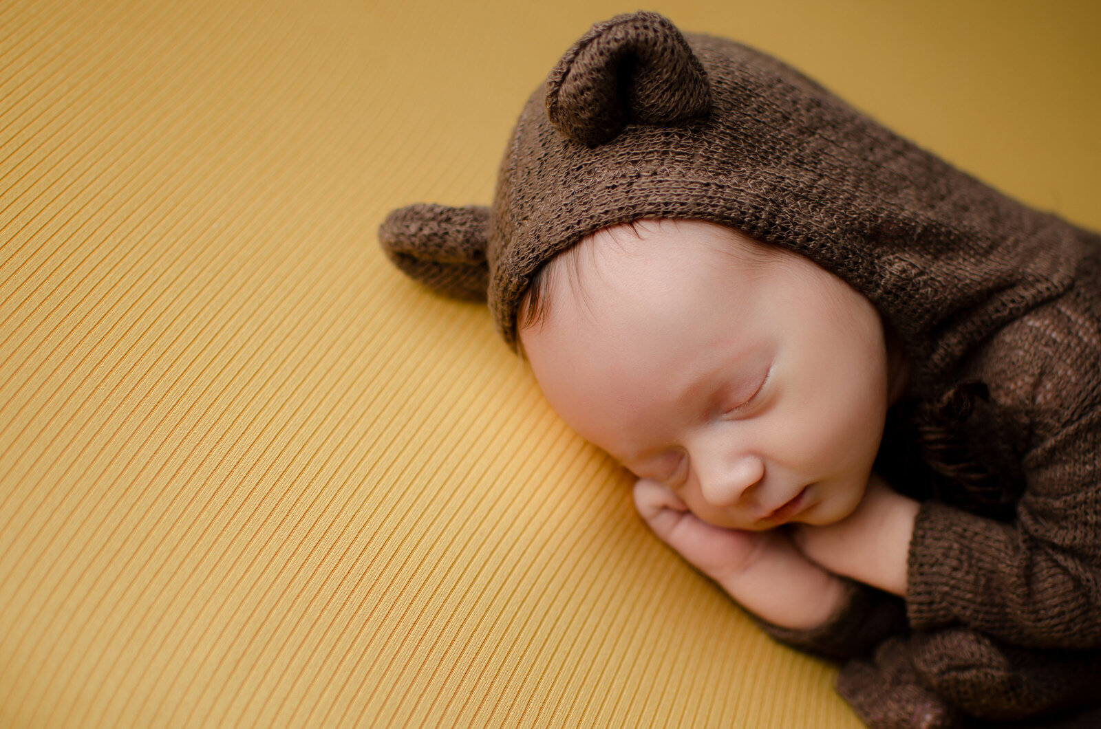 baby boy on yellow backdrop in cute bear outfit
