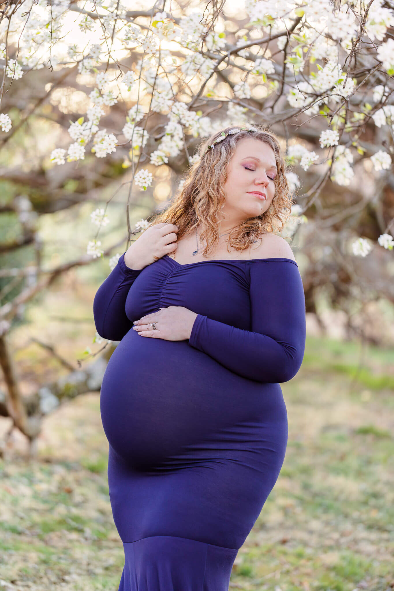 A mom-to-be holding her pregnant belly in front of blossoming tree.