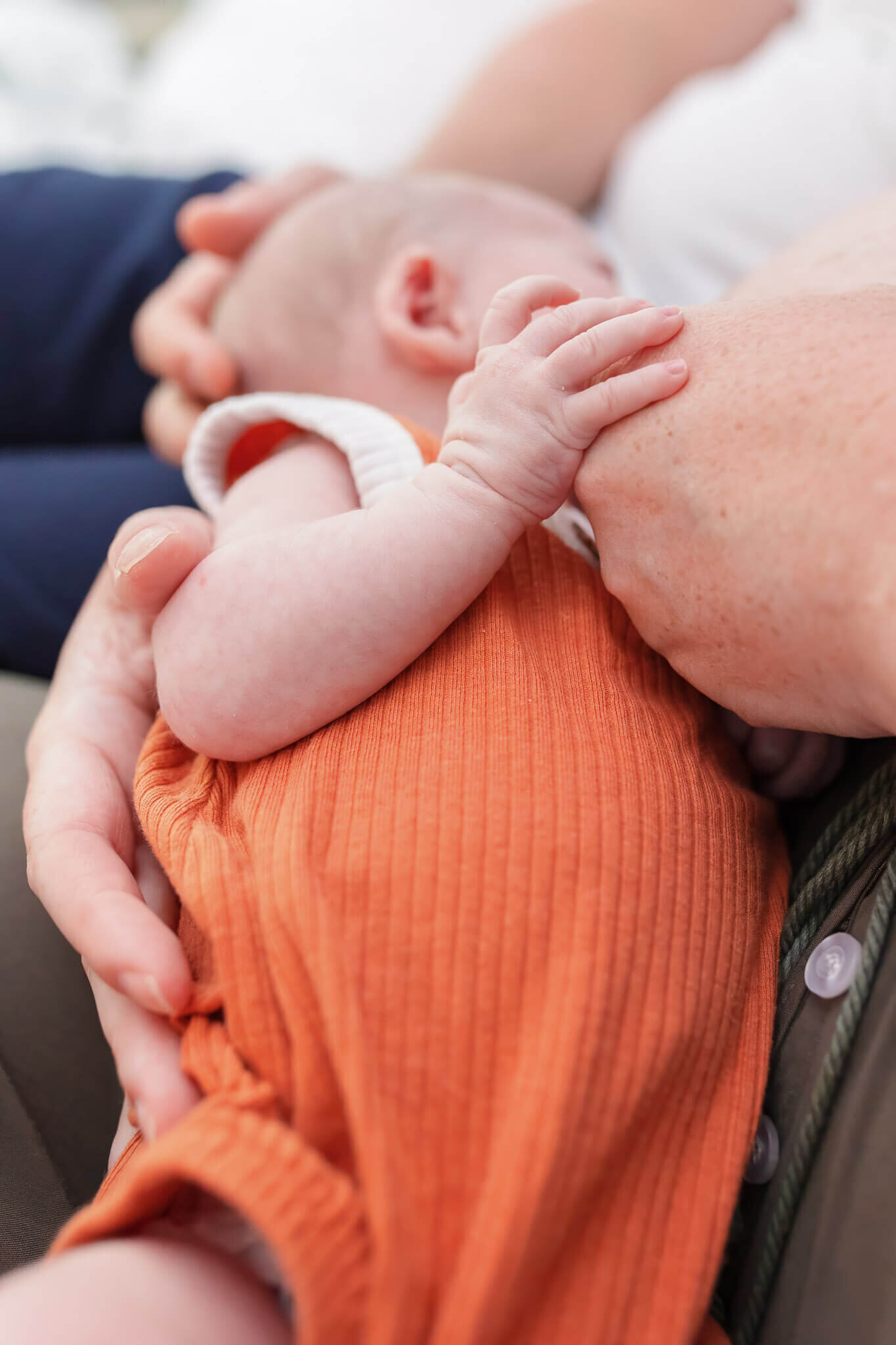 A close-up of a newborn boy nursing while holding mom's hand.