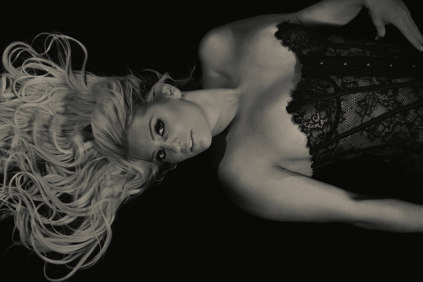 A gorgeous black and white boudoir image  of a blonde woman laying on the floor in a black Honey Birdette corset with old Hollywood glam lighting.