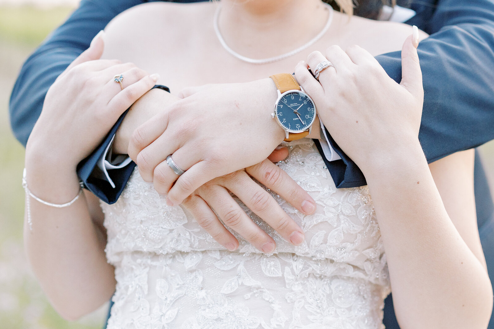 detail shot of groom wrappin ghis arms around his brides shoulders as he stands behind her while she reaches up to hold his arms for their california wedding pictures captured by sacramento wedding photographer