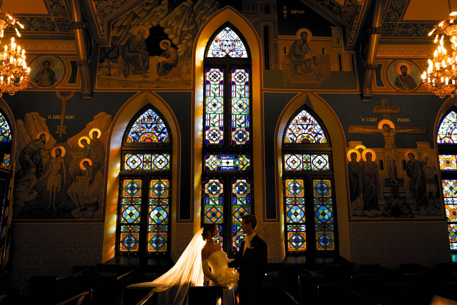 A bride and groom stand in front of a stained glass window