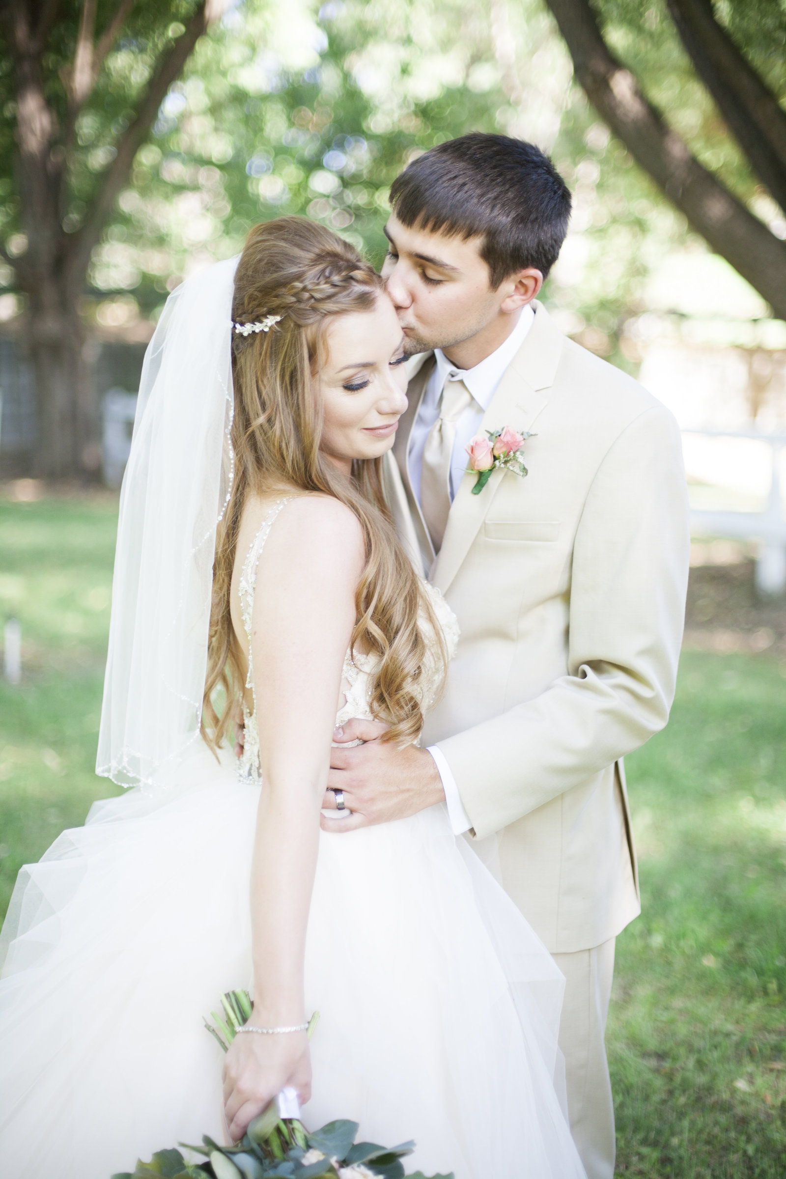 A groom kissing his bride on the forehead.