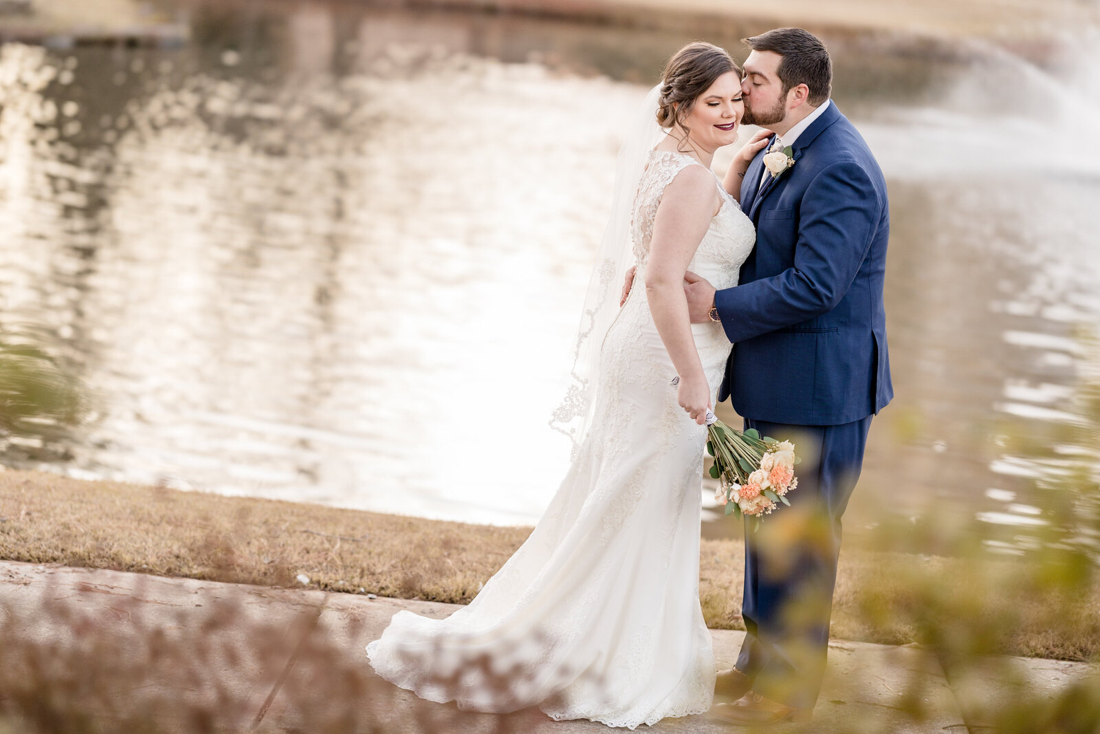 Groom kissing Bride in front of a lake