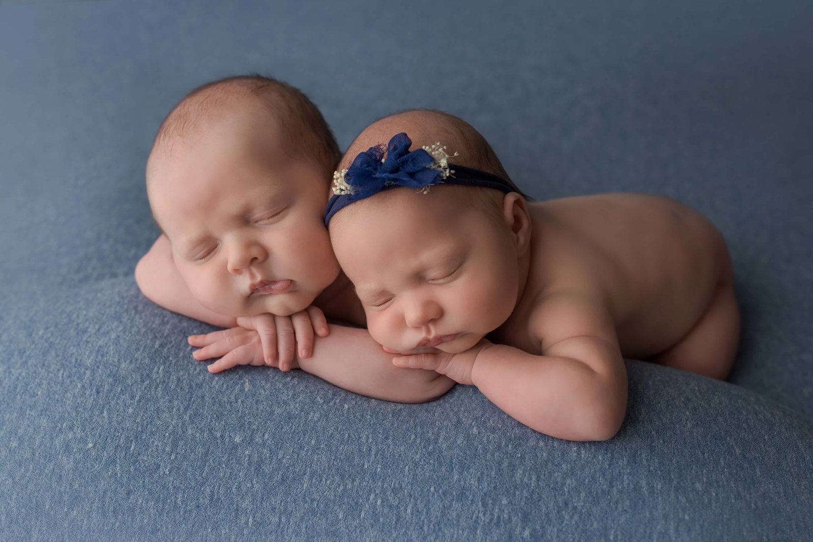 newborn twins sleeping posed with heads on hands lying on a blue blanket