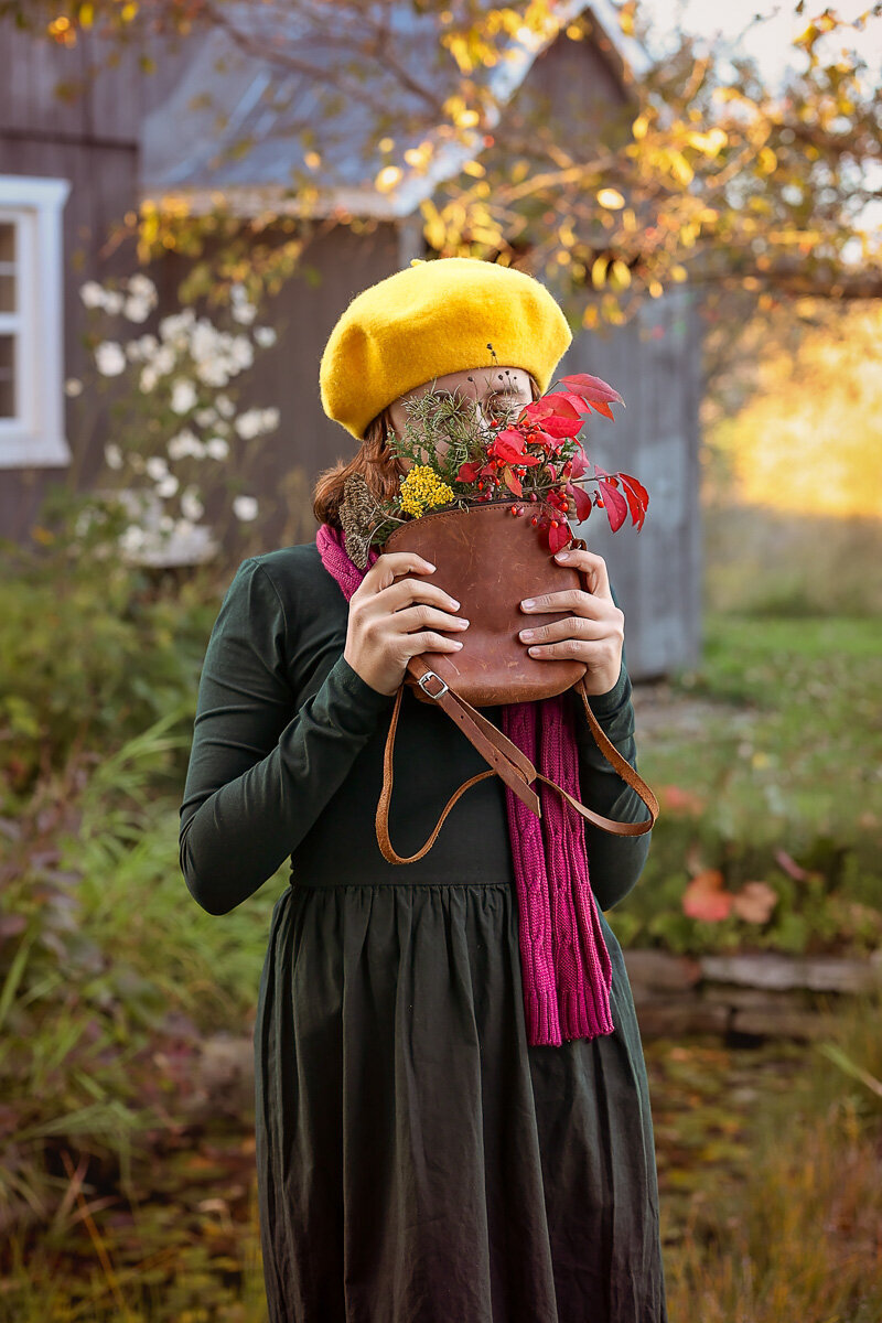 Girl smelling fall bouquet of flowers and wearing yellow biretta hat on the farm in Quebec by Yuliia Terziian Photography.