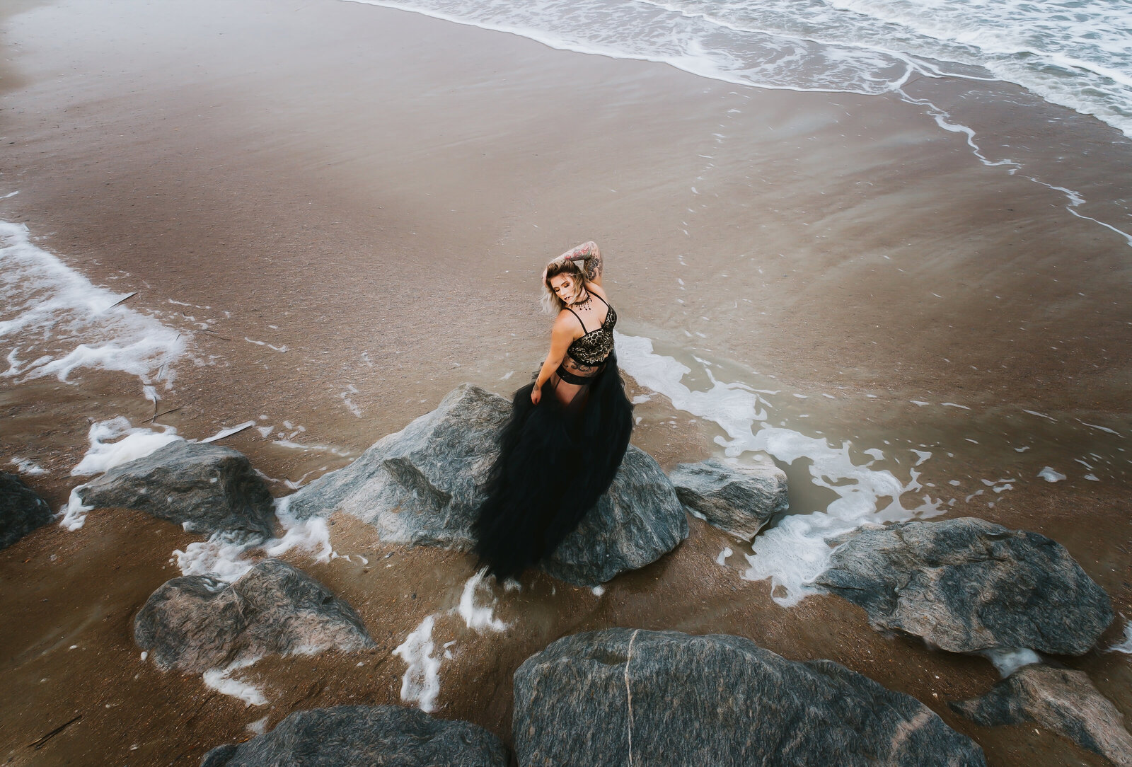 Aerial shot of woman on beach with black gown standing on jetty