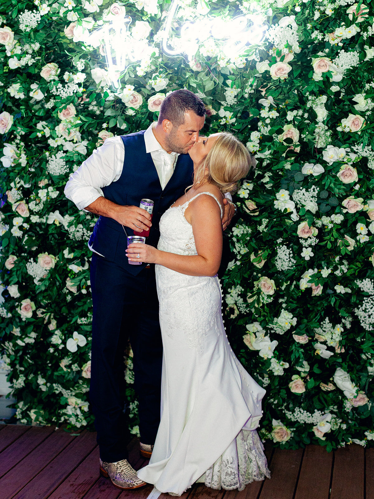 bride and groom kissing in font of a flower wall