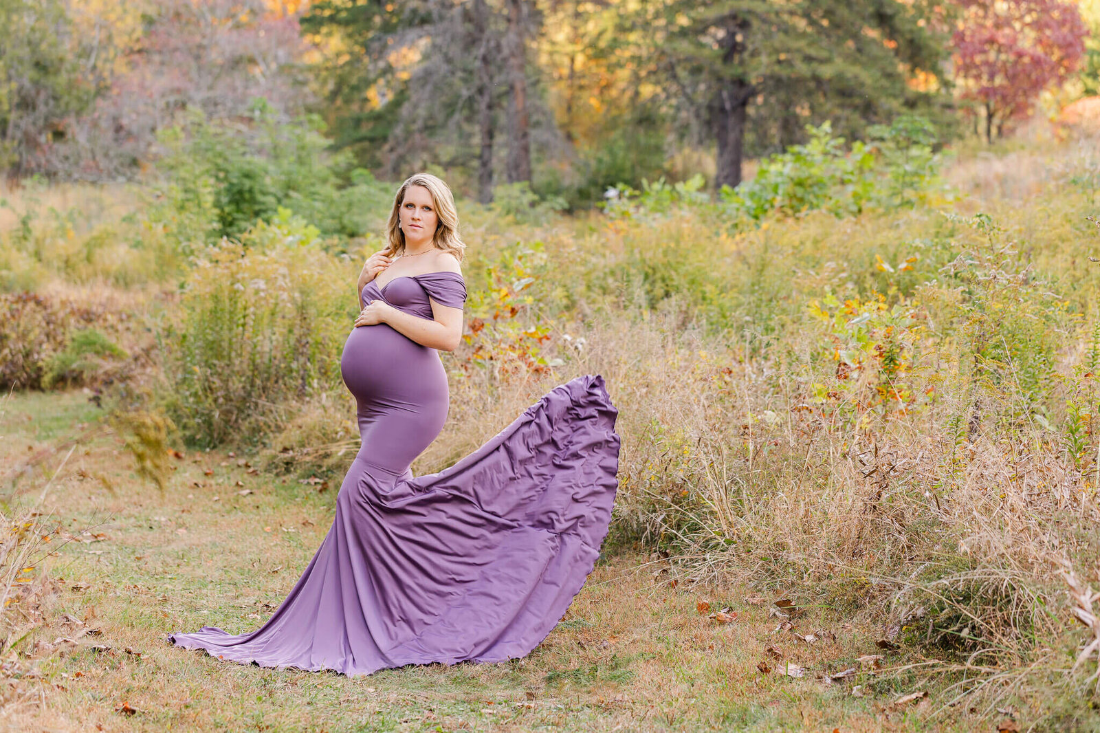 A pregnant woman in a field with her purple dress flying behind her