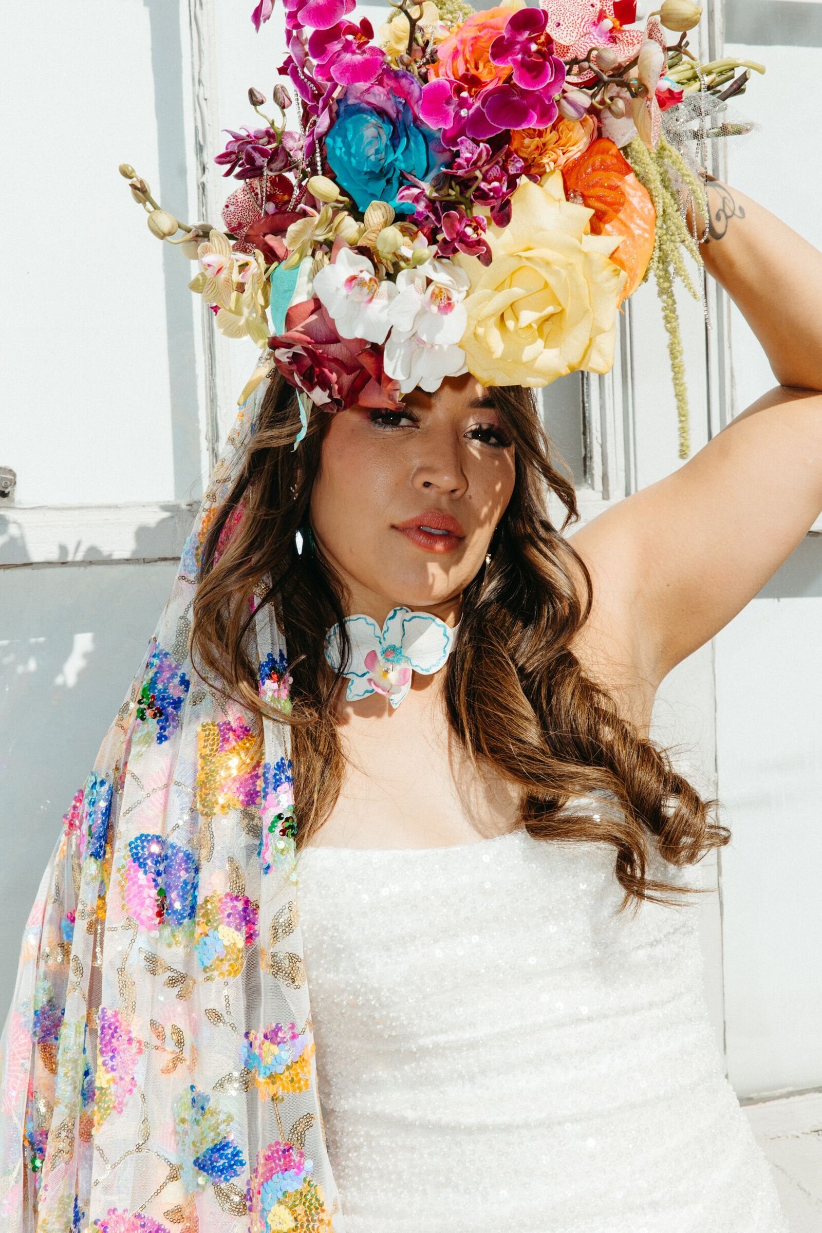 closeup of a bride wearing a white gown and a colorful sequined veil holding her bouquet 