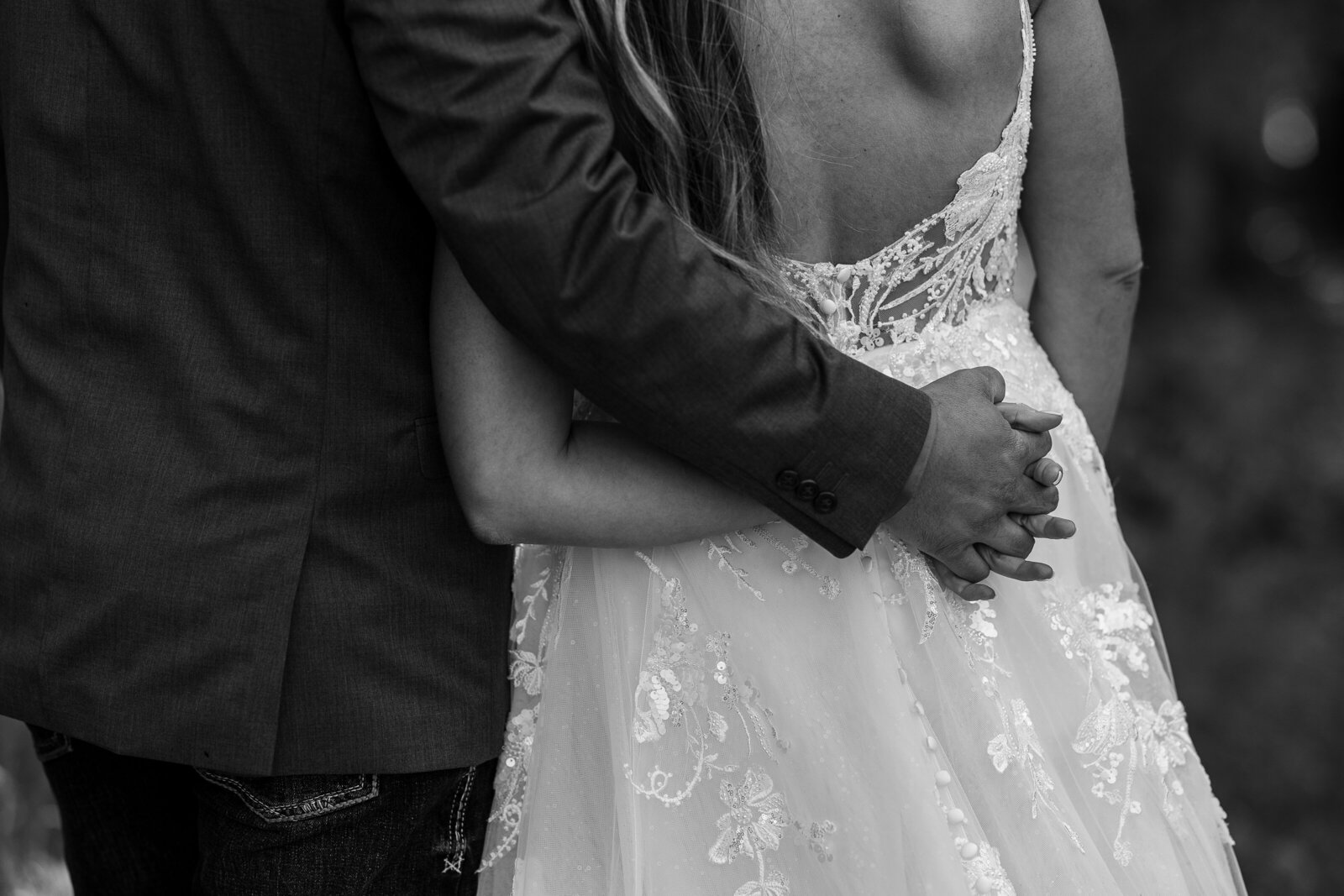 Black and white detail image of bride and groom holding hands beind brides back