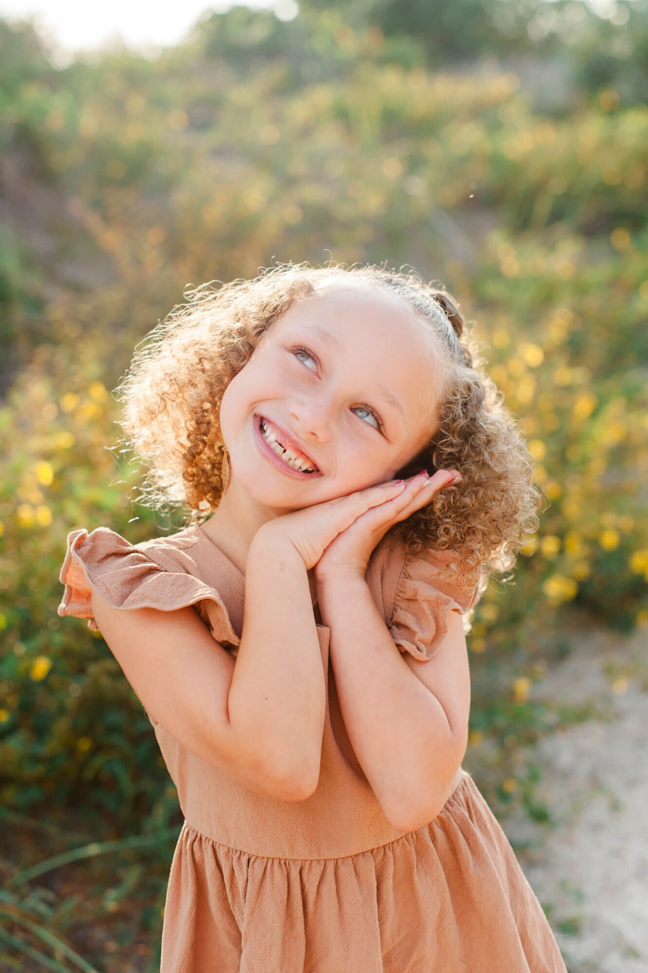 Young girl smiling and posing near beautiful yellow flowers at sunset