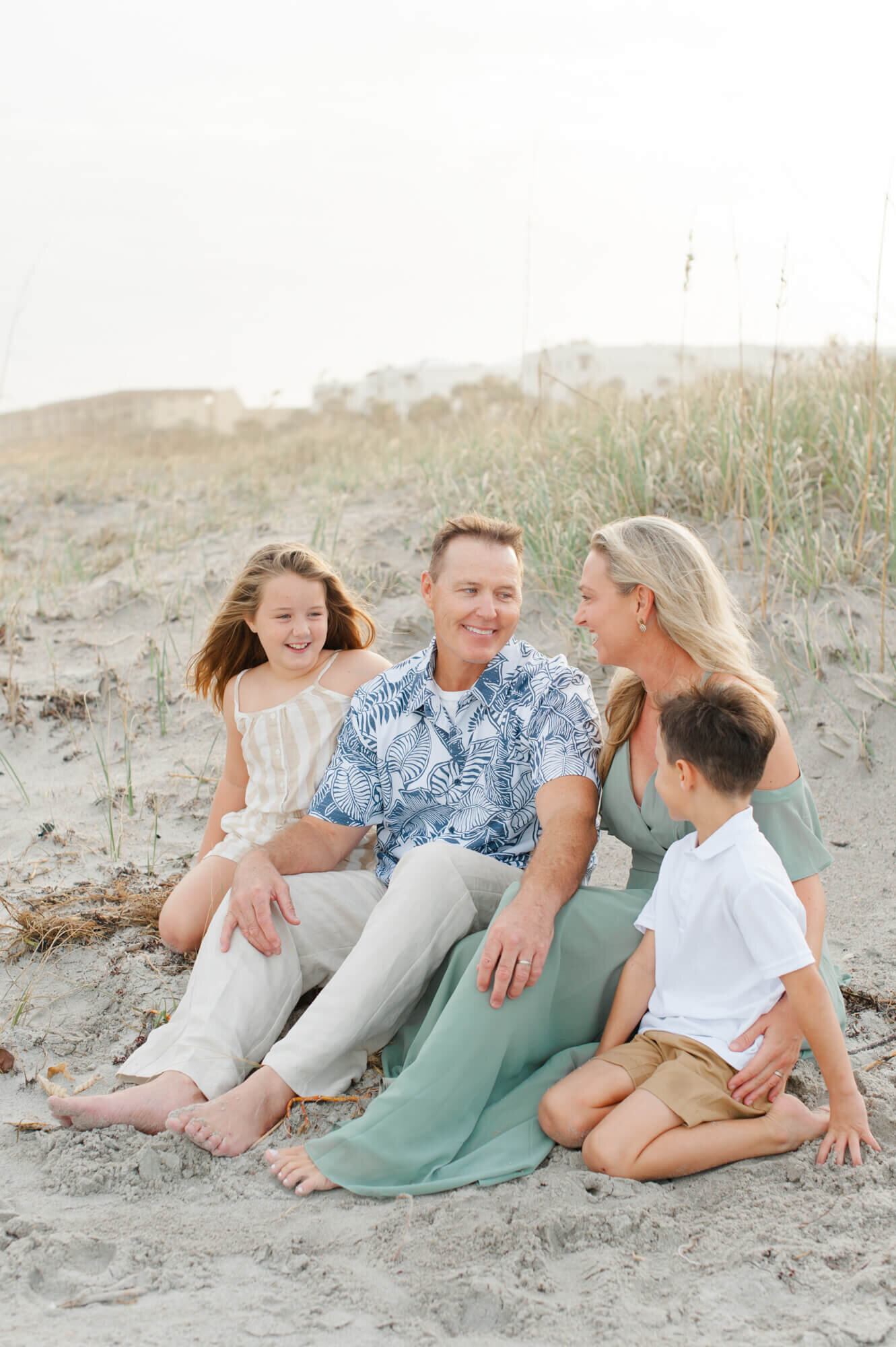Family sitting near the dunes laughing at each other at sunset