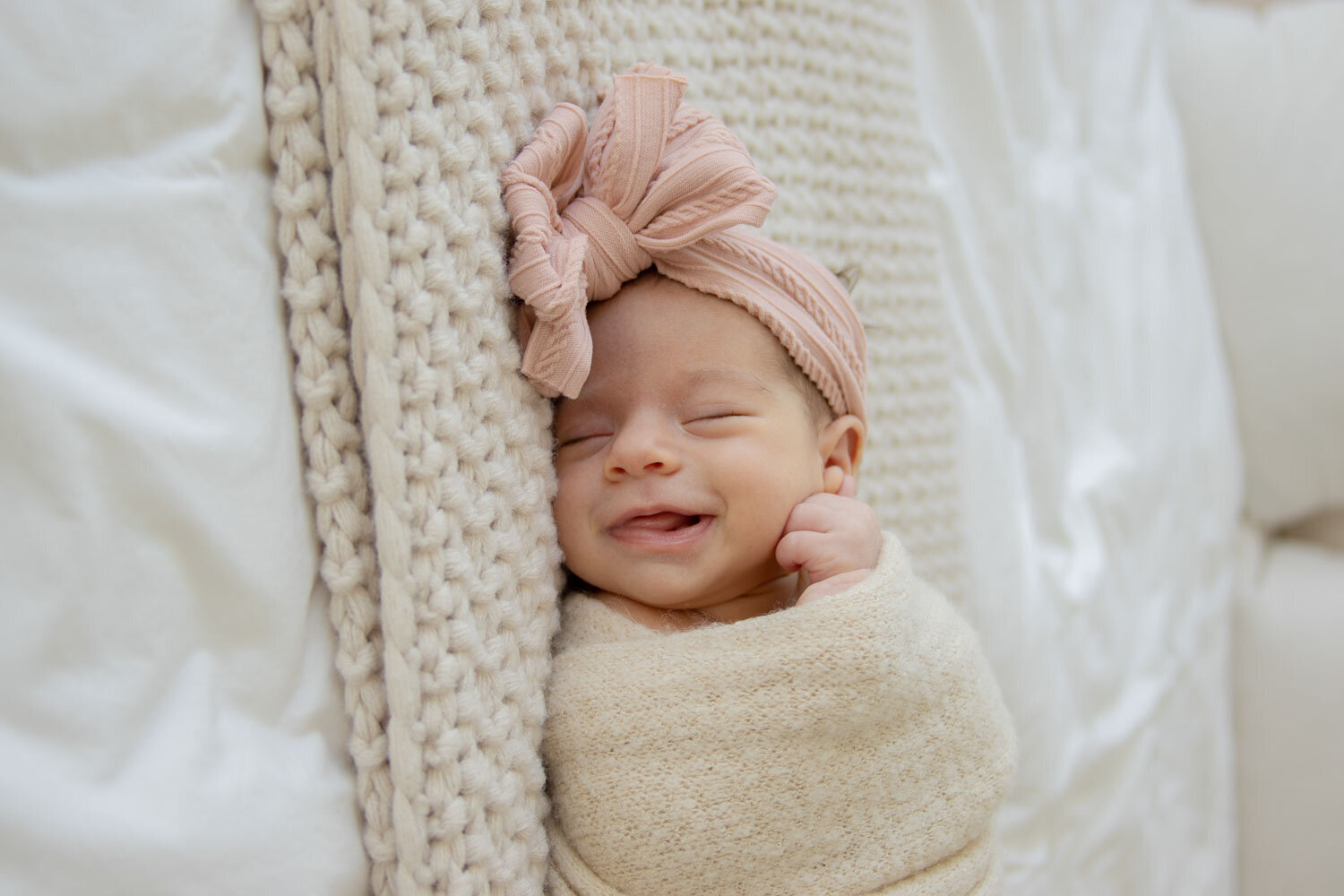 Smiling newborn baby girl wrapped in a blanket with a pink bow headband
