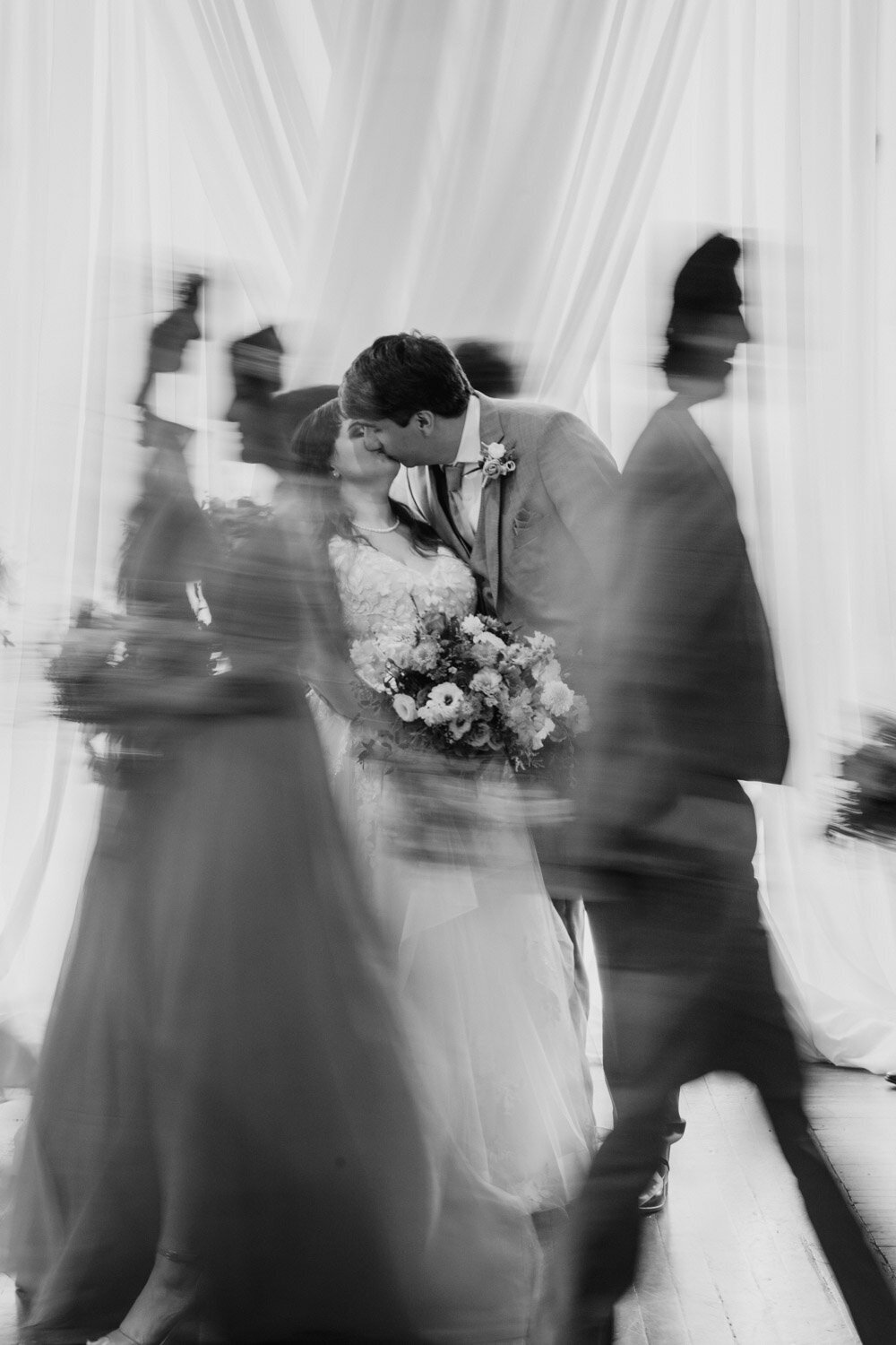 Bride and groom kissing while guests walk past in motion blur