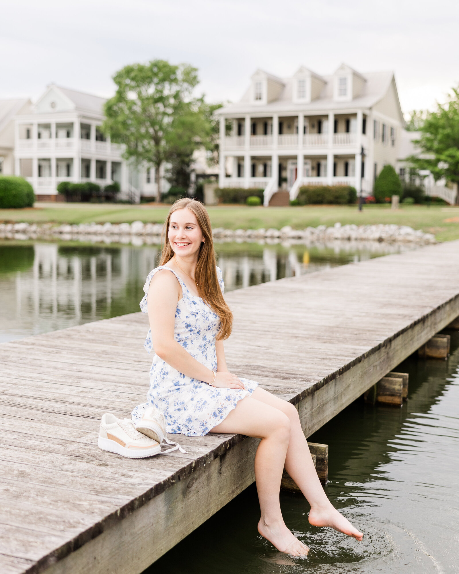 Sophie sitting on a wooden dock with her feet in the water, wearing a blue floral dress, captured by Abby Bell Photography, Fine Art Portrait Photographer based in Alabama.