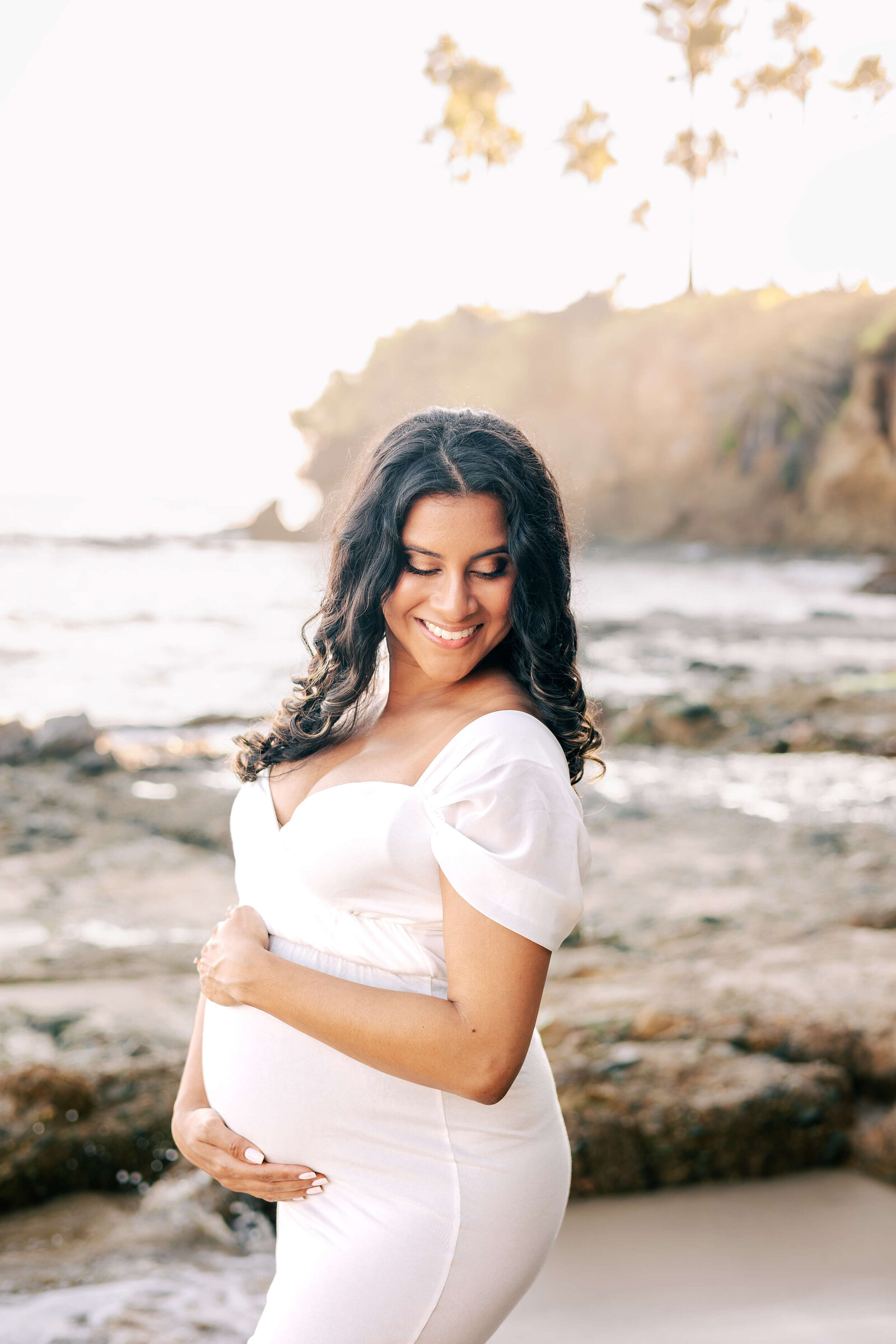 Expectant mom smiling looking over her shoulder in Laguna Beach maternity by Ashley Nicole Photography.