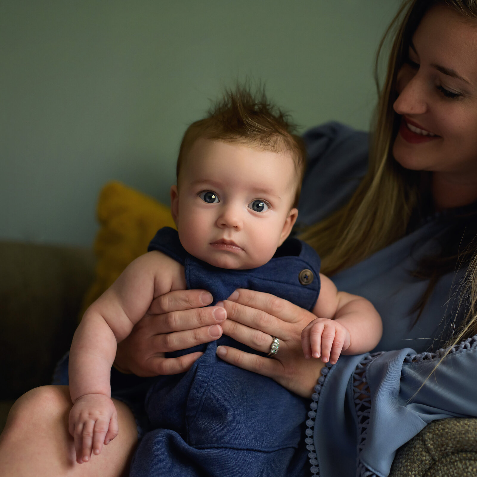 baby boy in blue overalls sitting on mom's lap staring at the camera